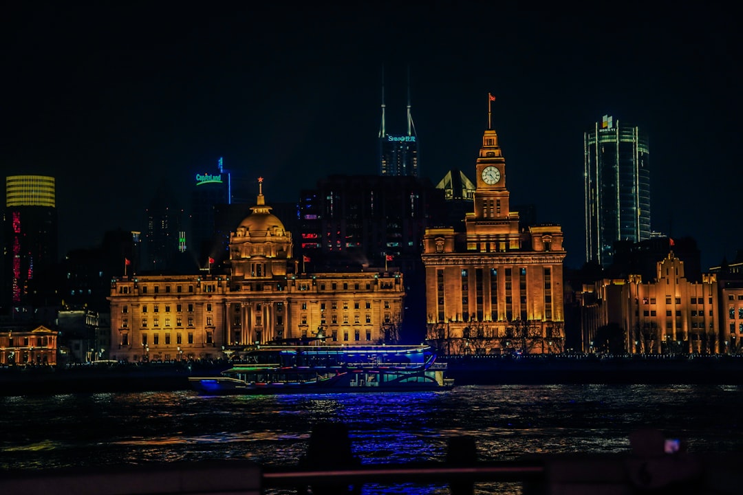 Shanghai Bund night view with colonial heritage buildings in foreground and illuminated Pudong skyline across the Huangpu River, boat cruising on the river