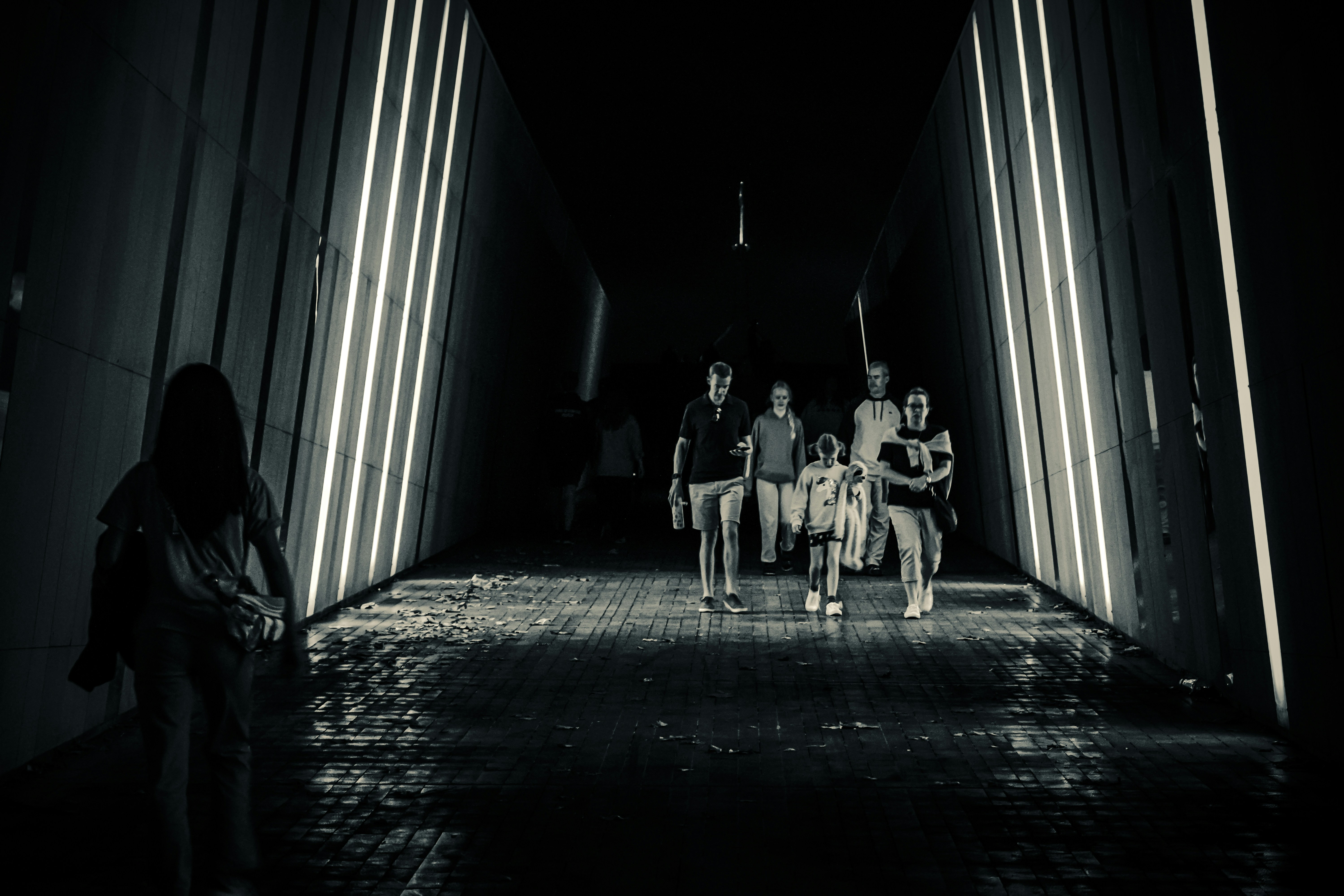 As pessoas caminham por um túnel escuro, iluminado por luzes.