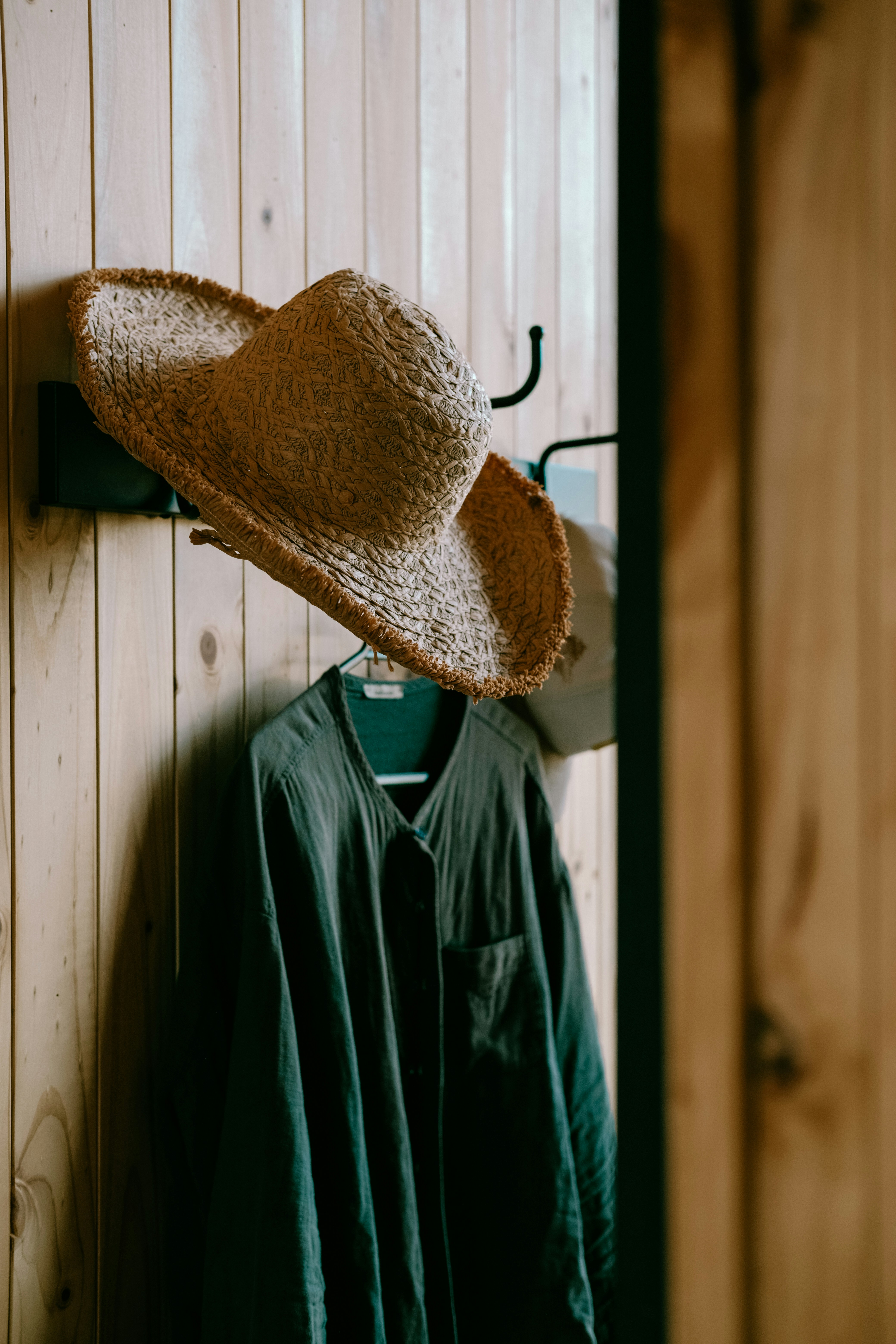 A hat and coat are hanging on a wooden wall.