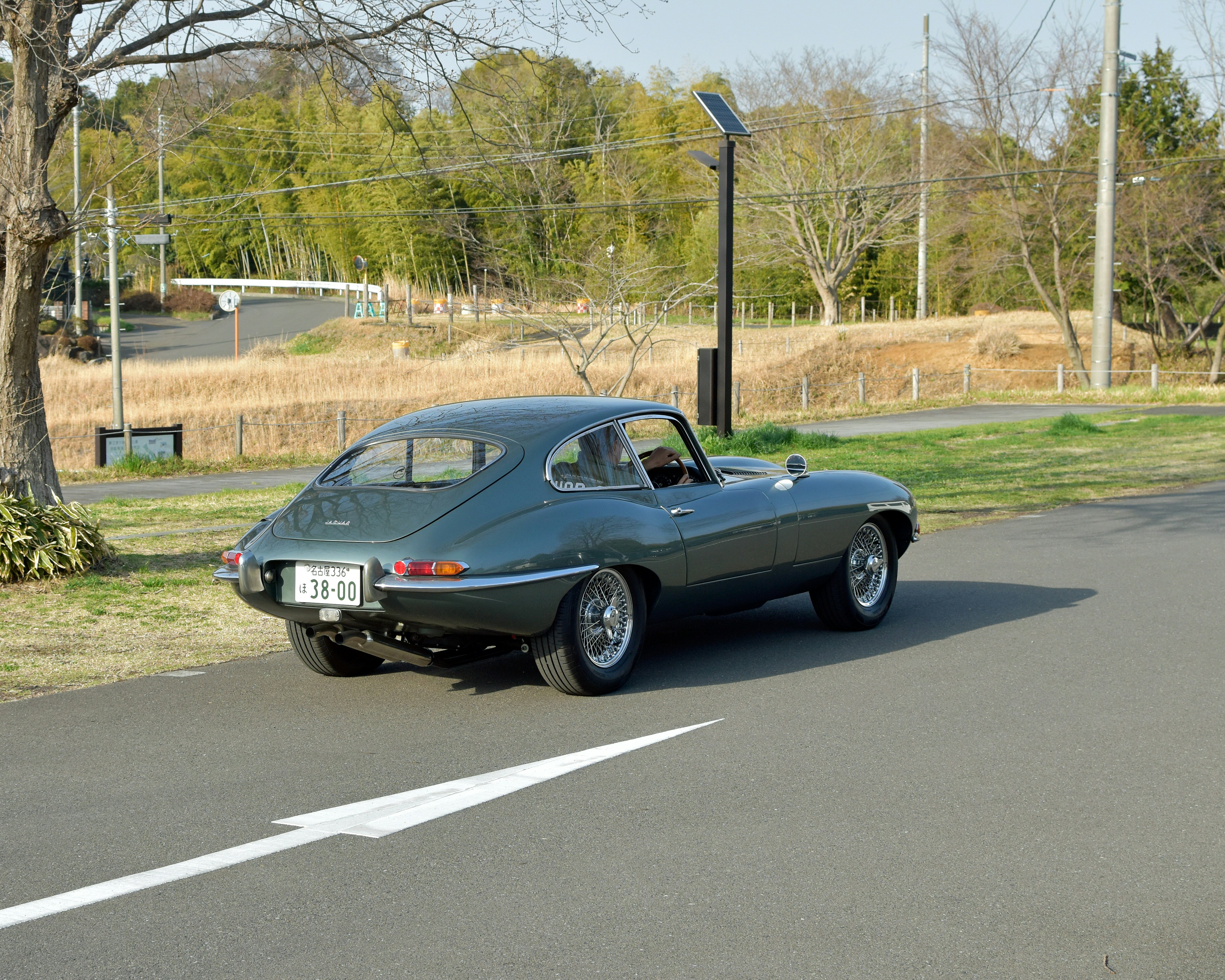 A classic green jaguar is on the road.