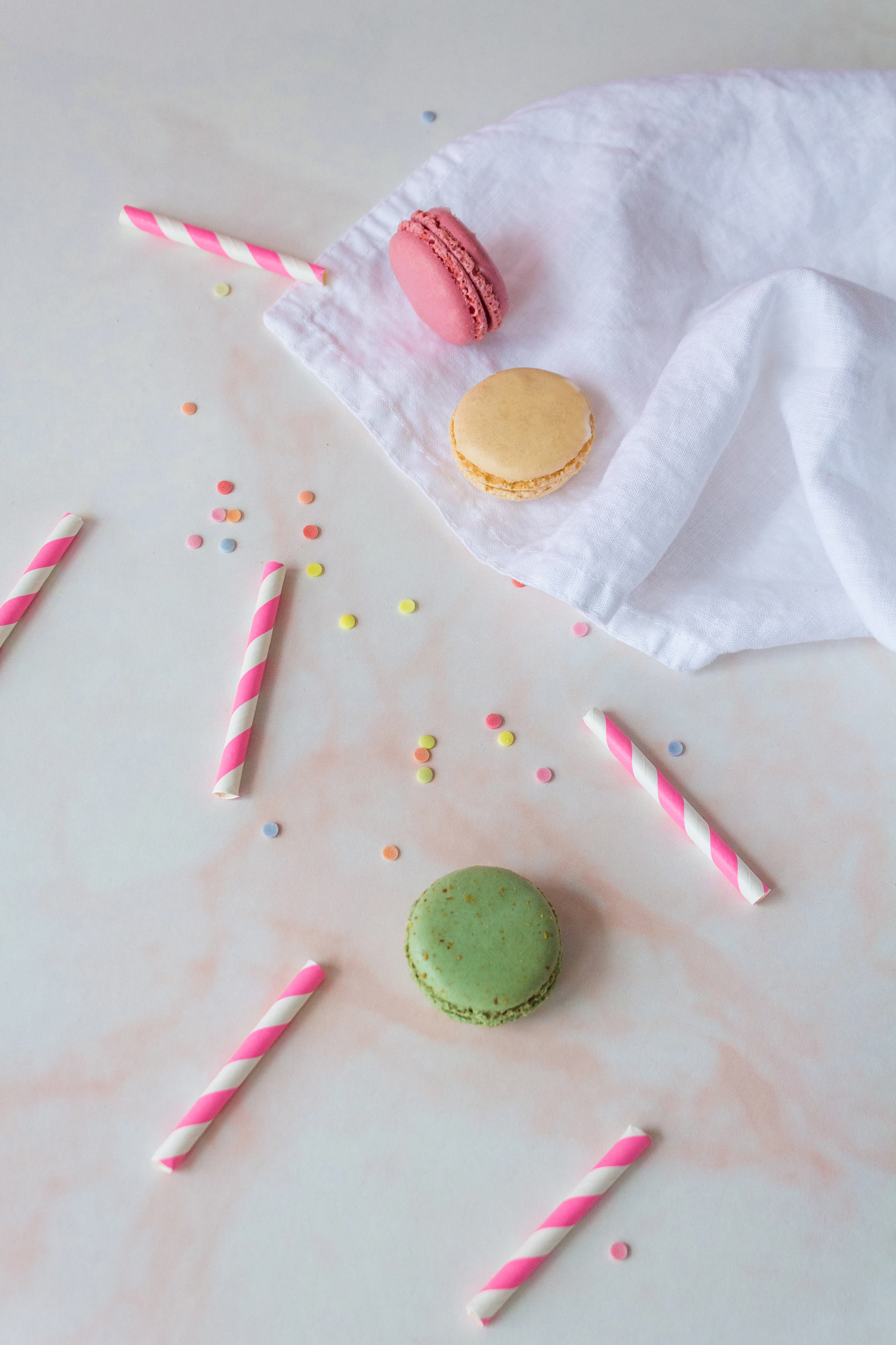 Macarons, straws, and sprinkles on a pastel surface.