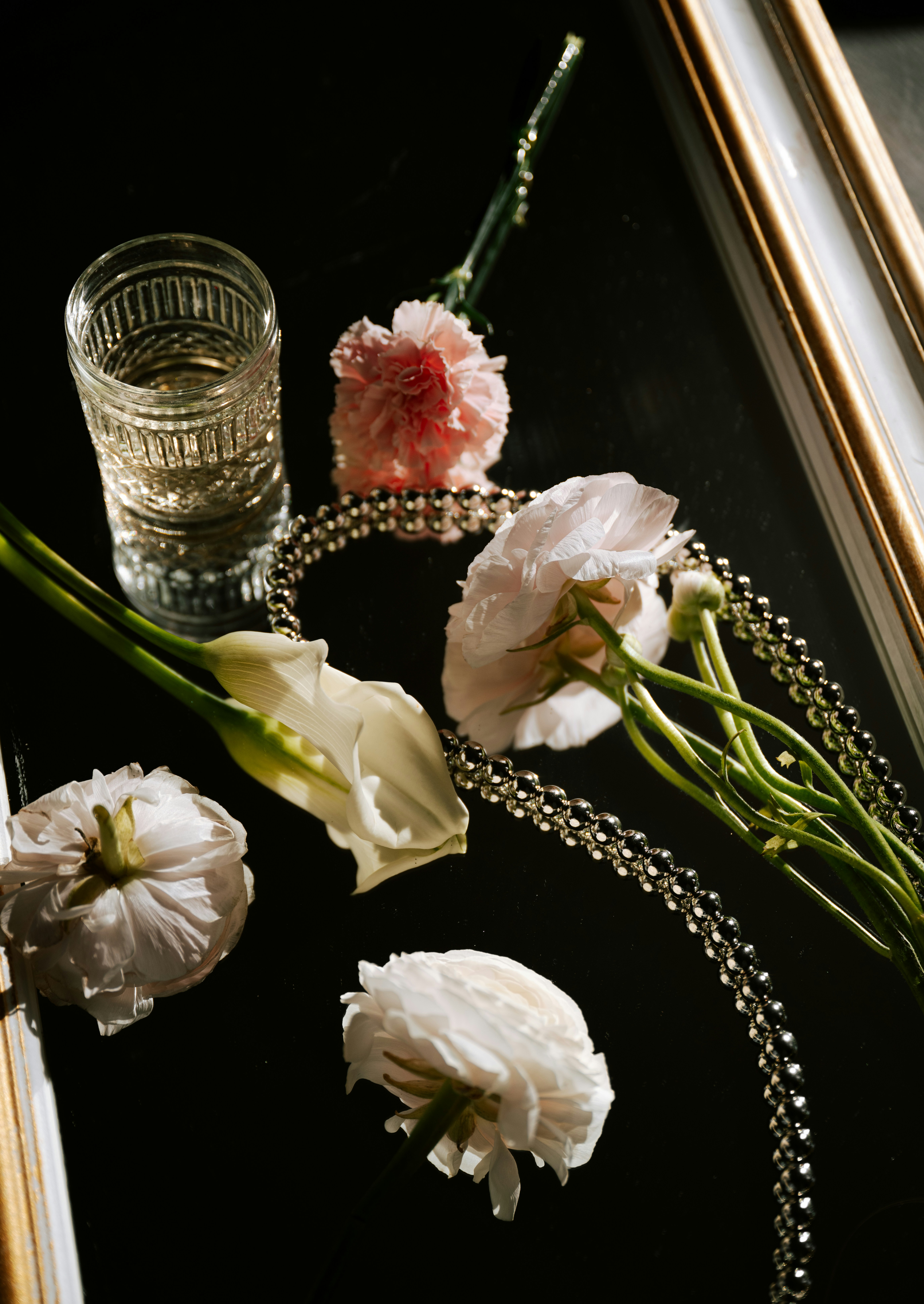 Flowers, glass, and jewelry on a black surface.