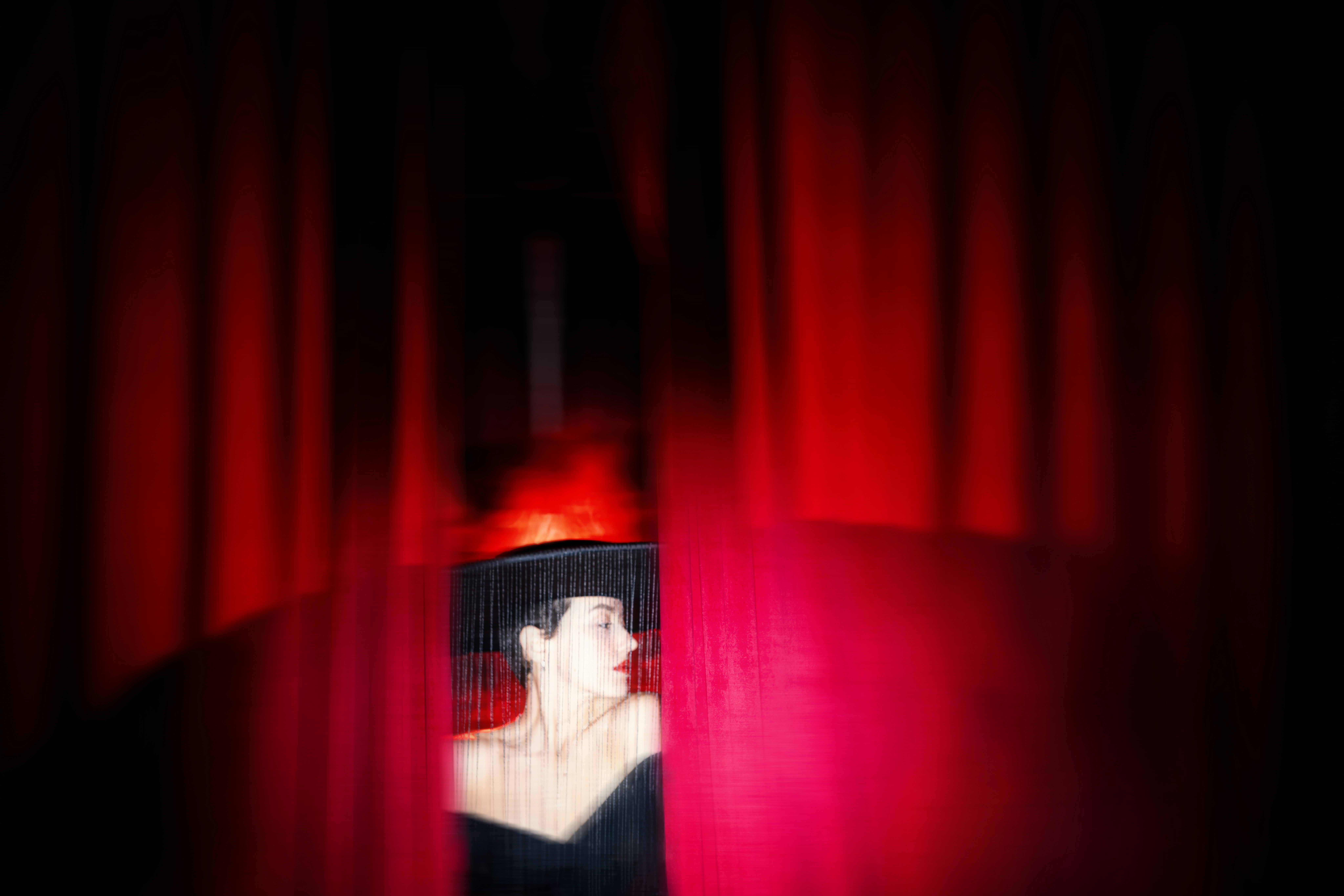 Une femme jette un coup d’œil derrière des rideaux rouges.