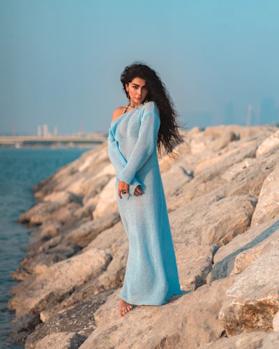 A woman poses on rocks, by the sea.