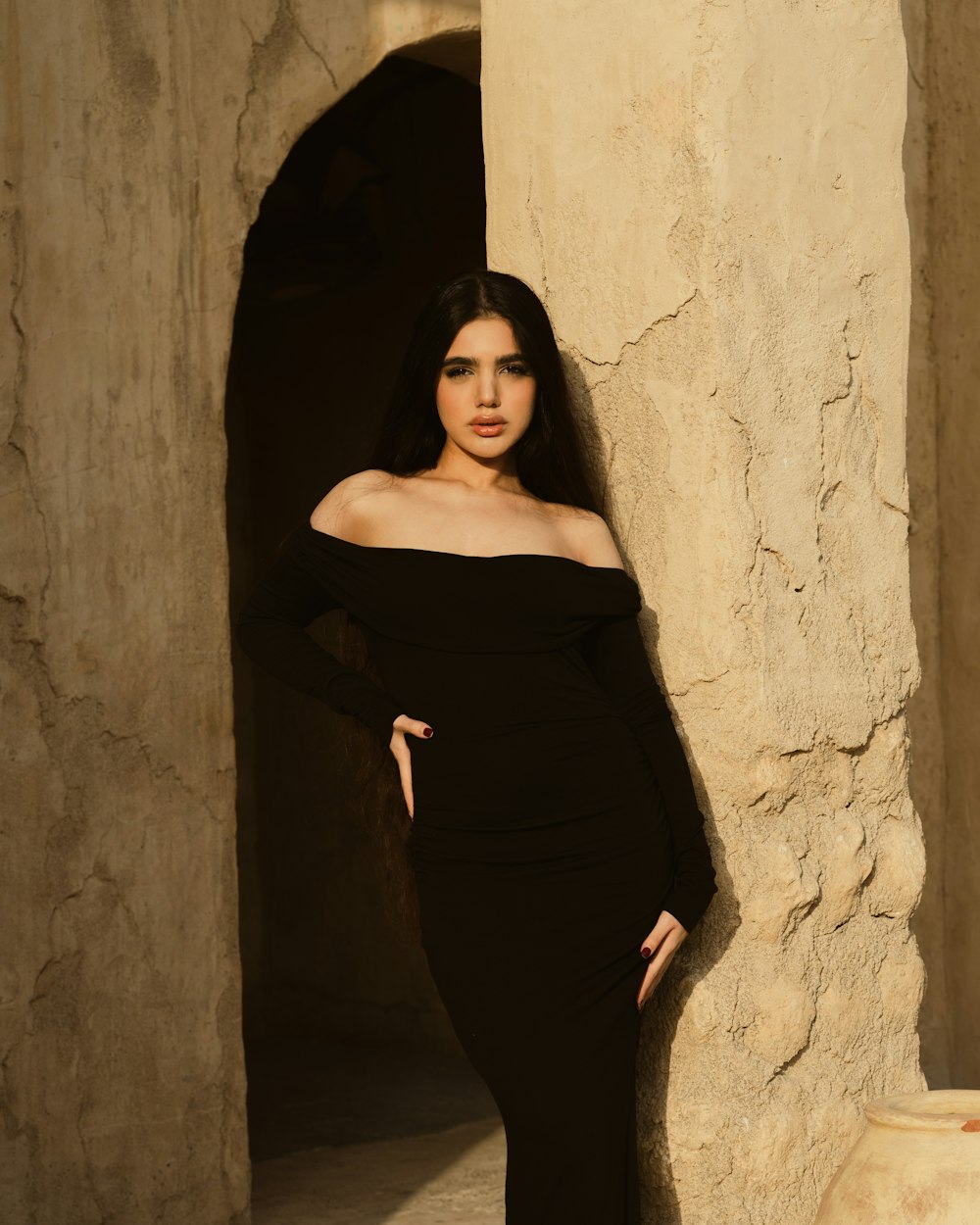 Model wearing a long black dress against a weathered stone wall