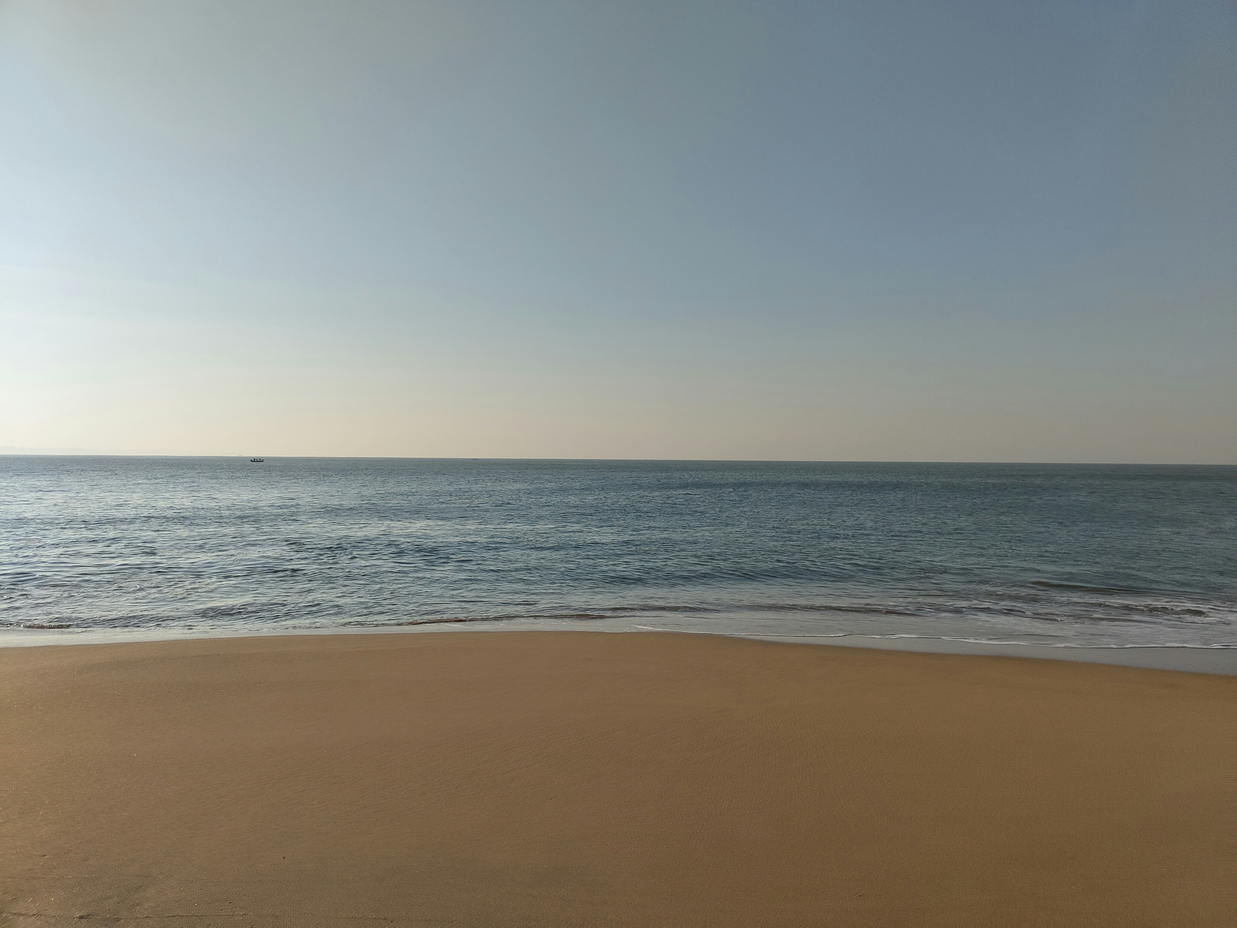 A sandy beach meets the ocean under a blue sky.