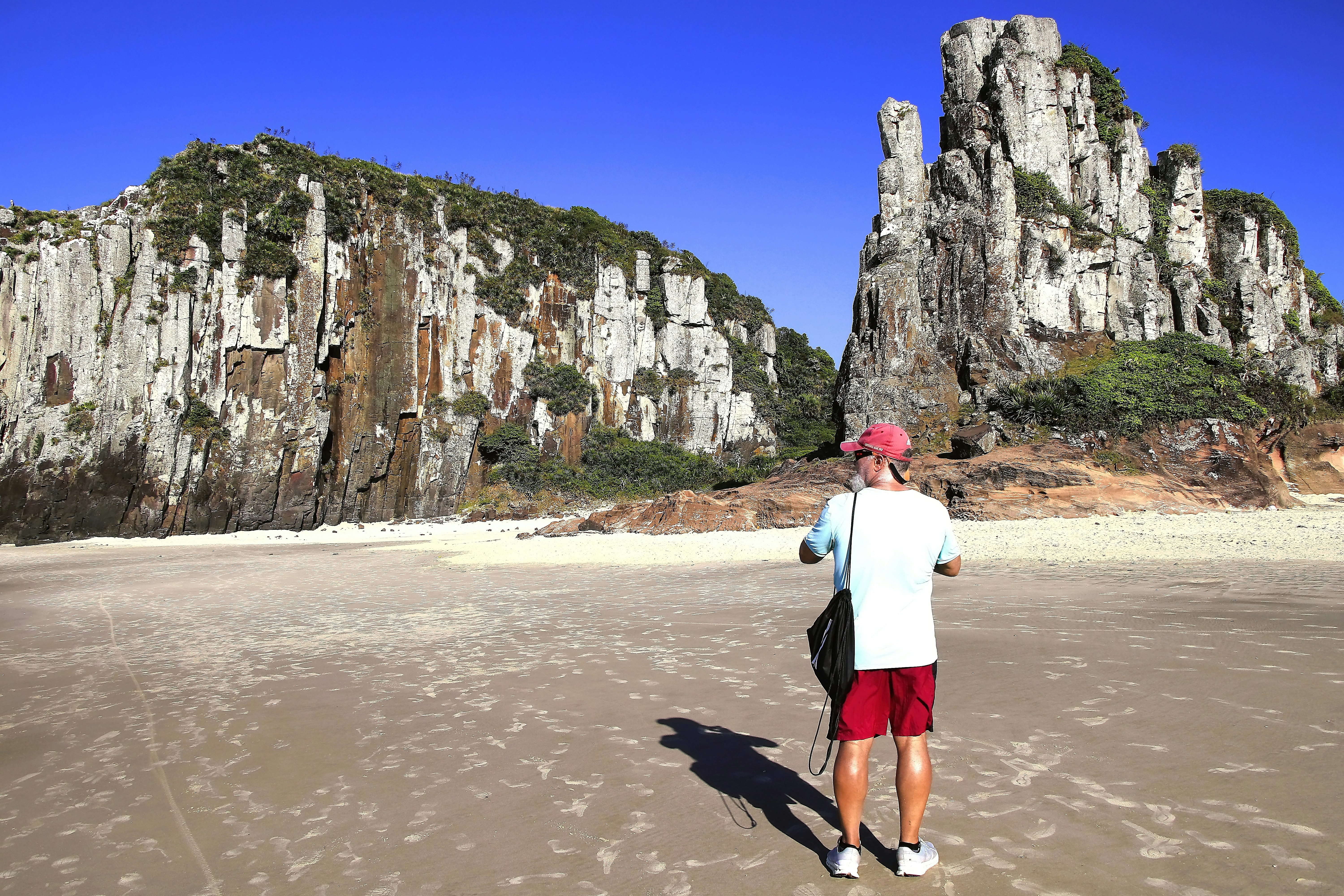Uma pessoa está diante de penhascos na praia.