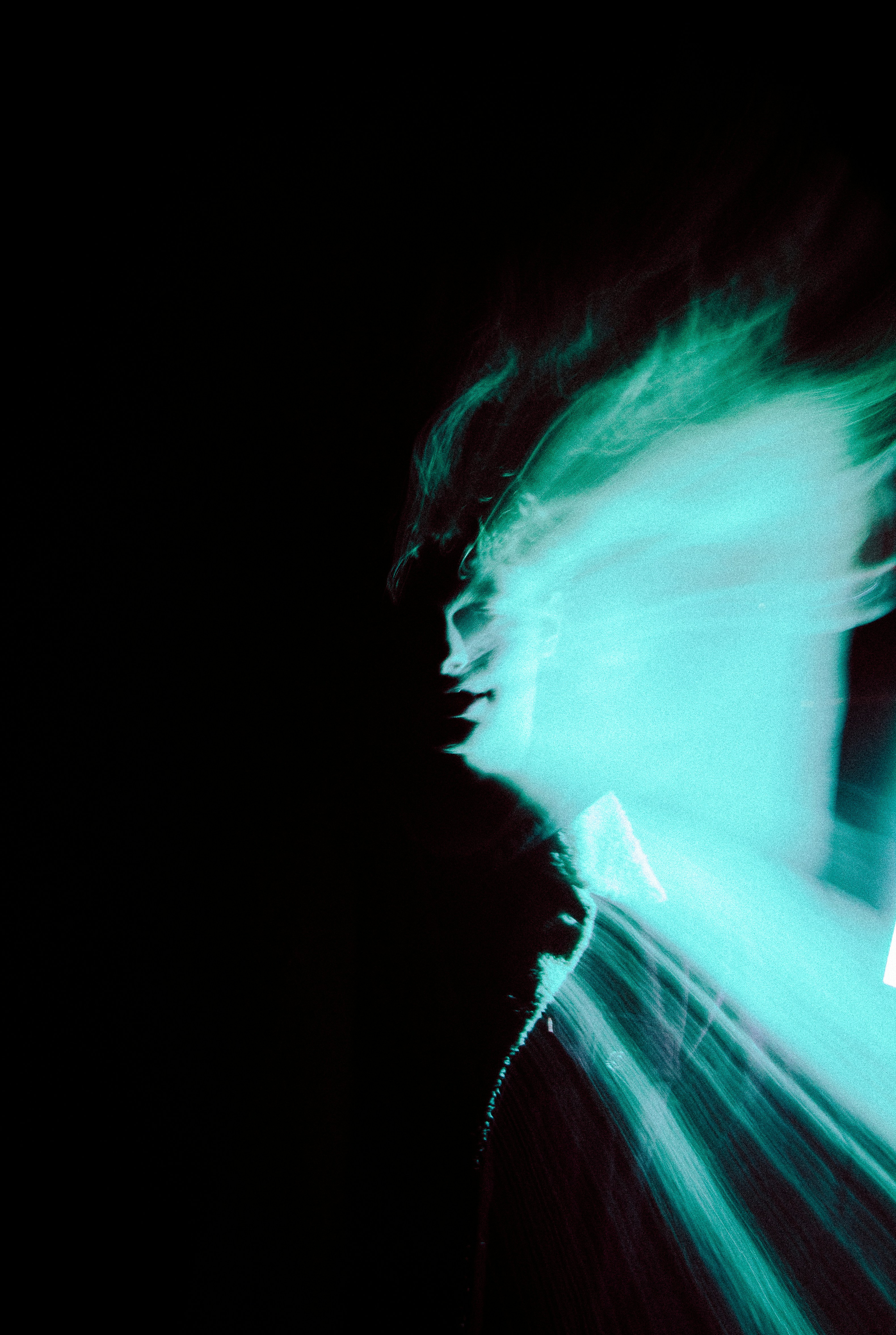Blurred figure glows in cyan against a black background.