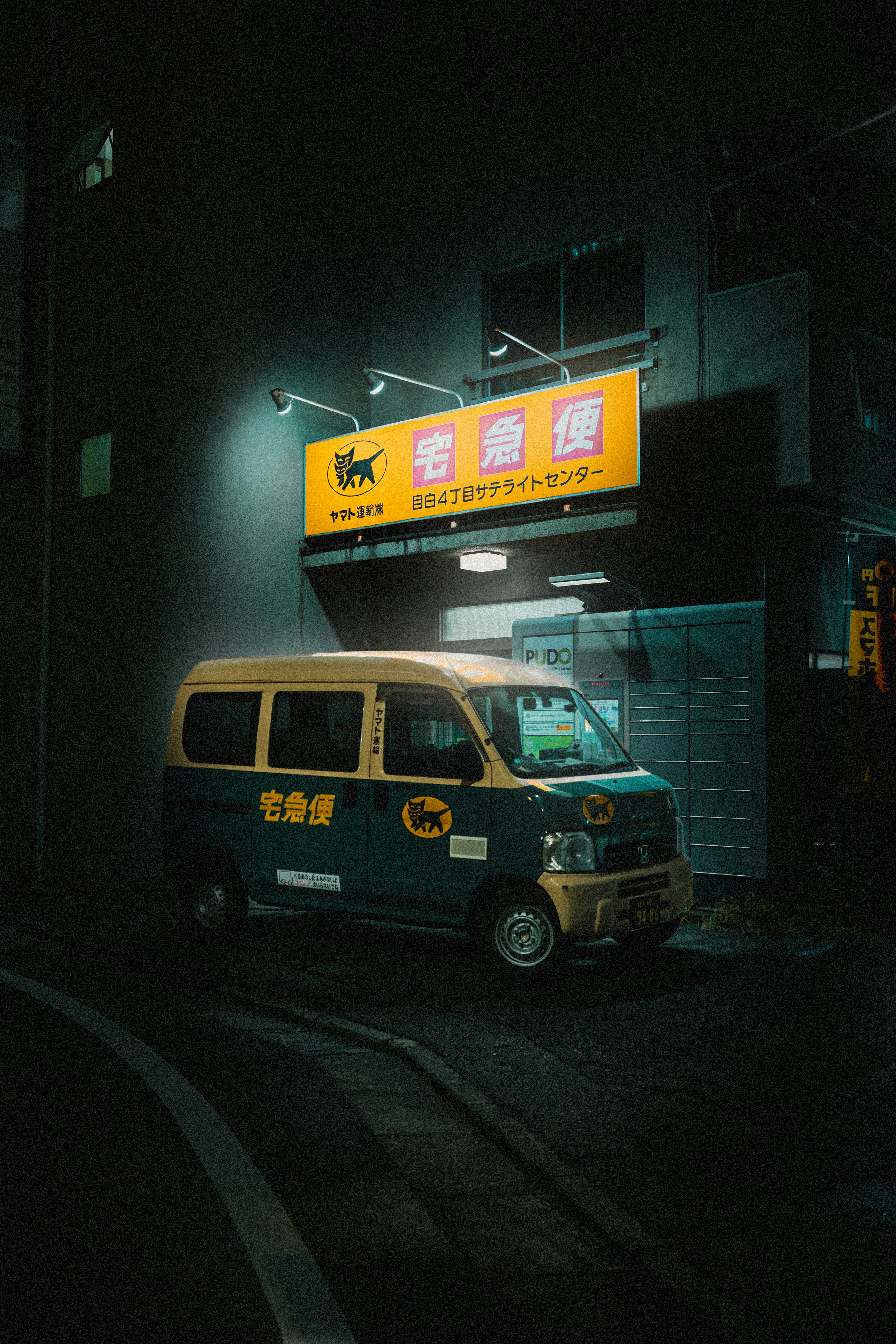 A japanese delivery van sits under a bright sign.
