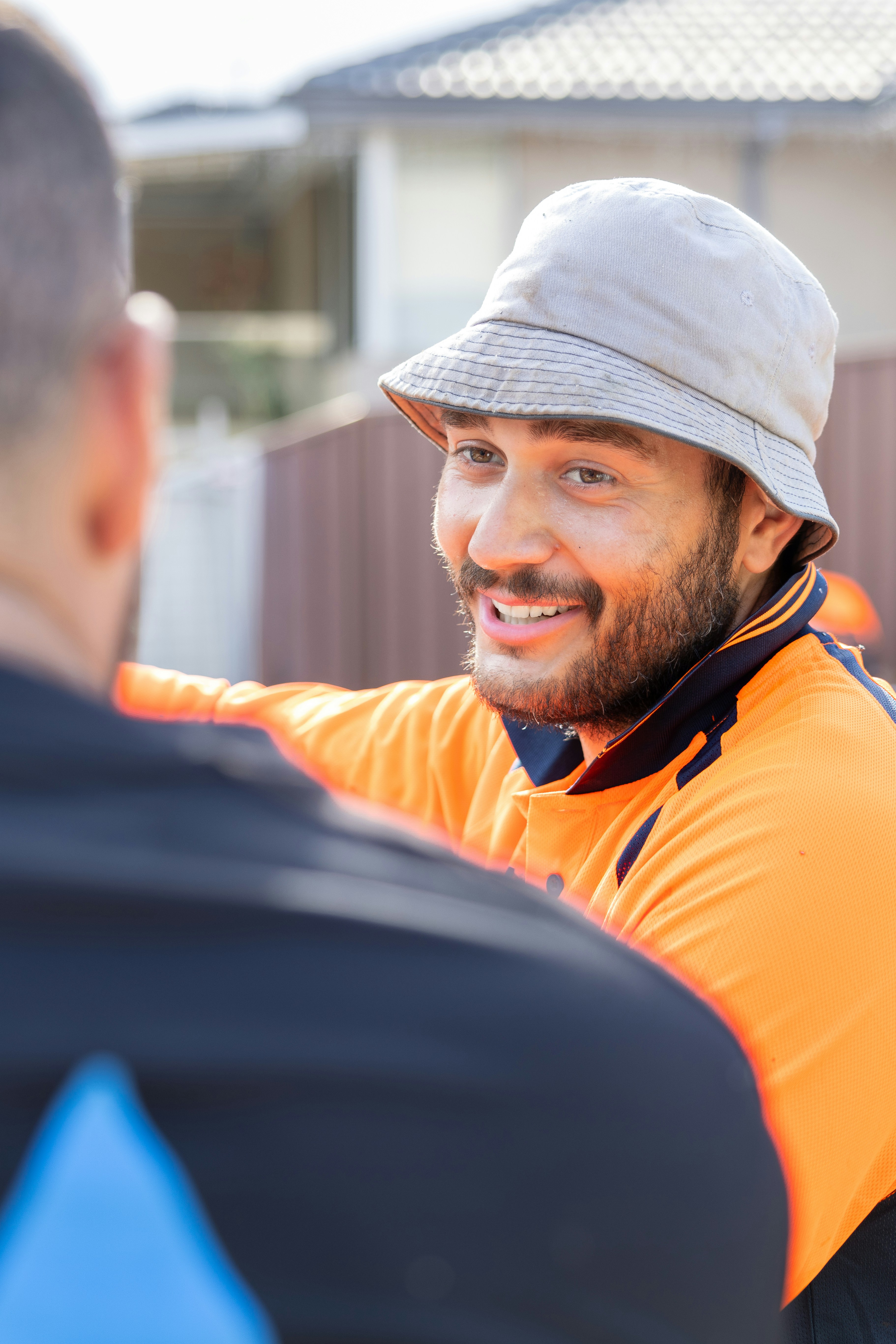 Man in orange shirt smiles at another.