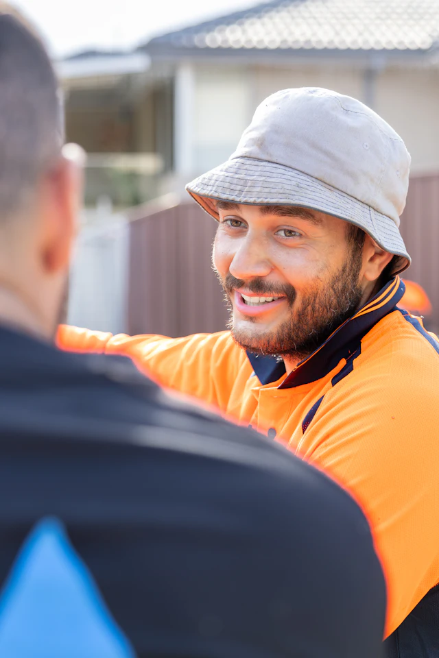 Two Australian tradespeople in hi-vis talking on a job site