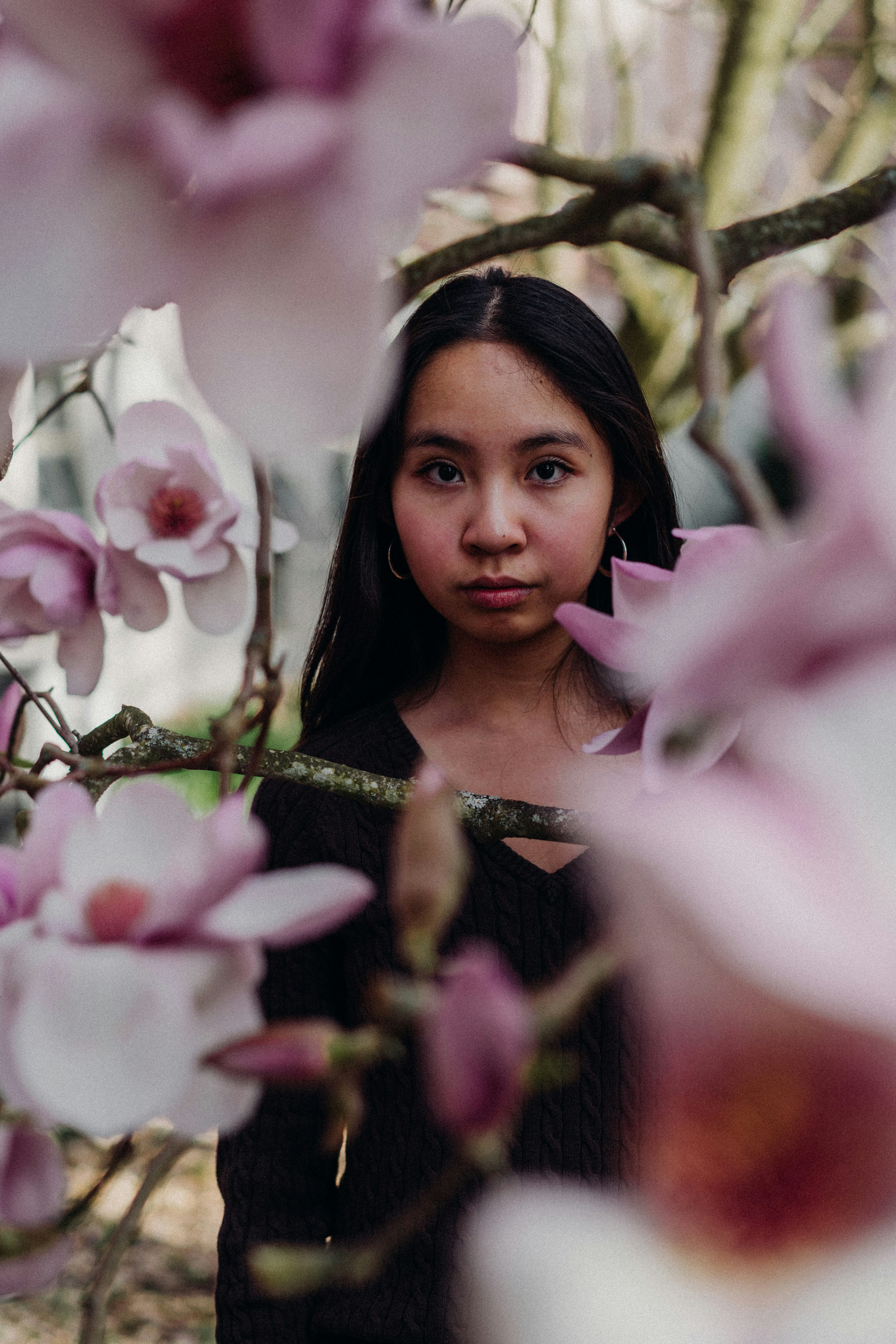 A woman gazes from behind blooming pink flowers.
