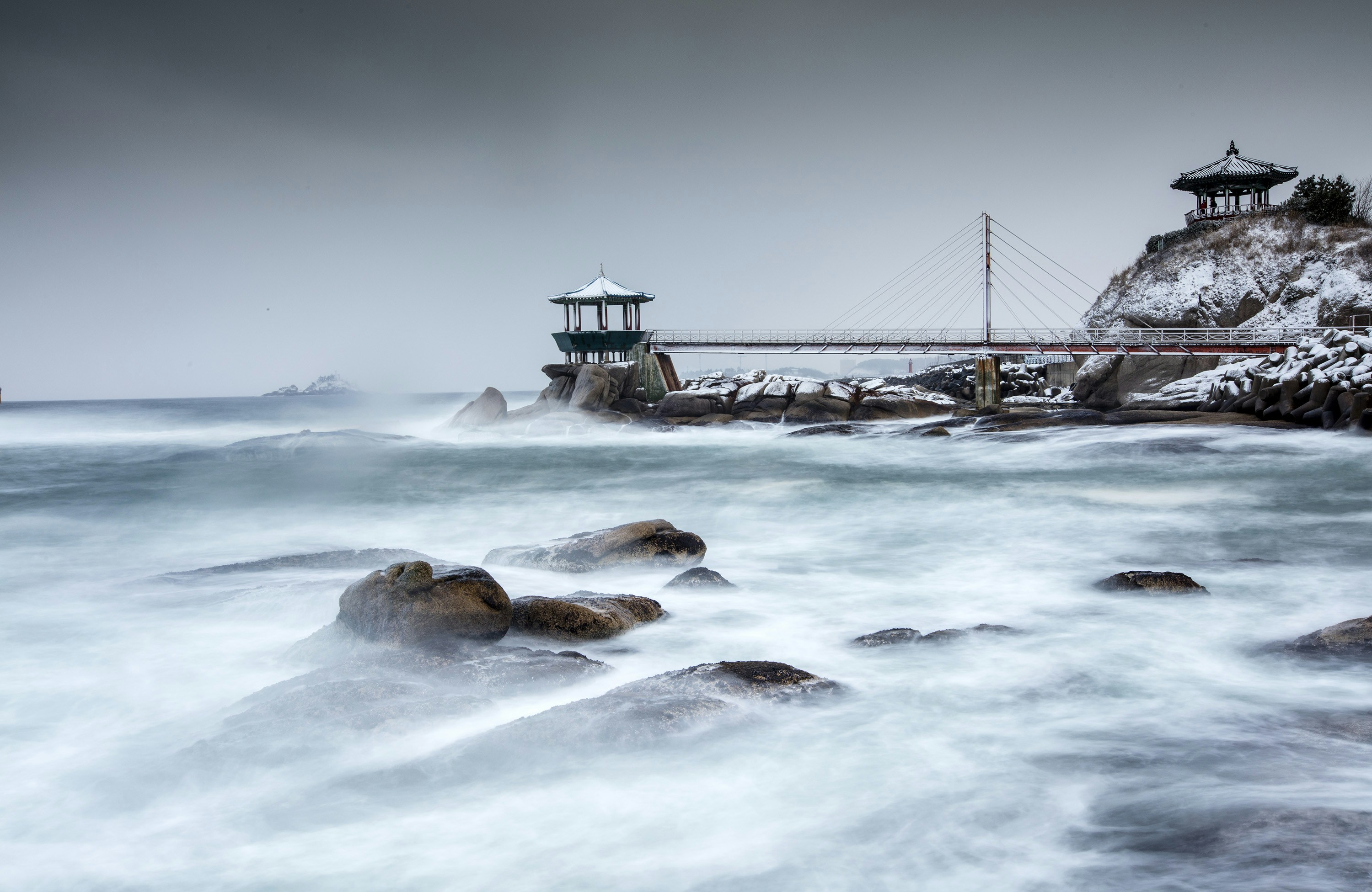 Waves crash near a structure on a rocky coast.