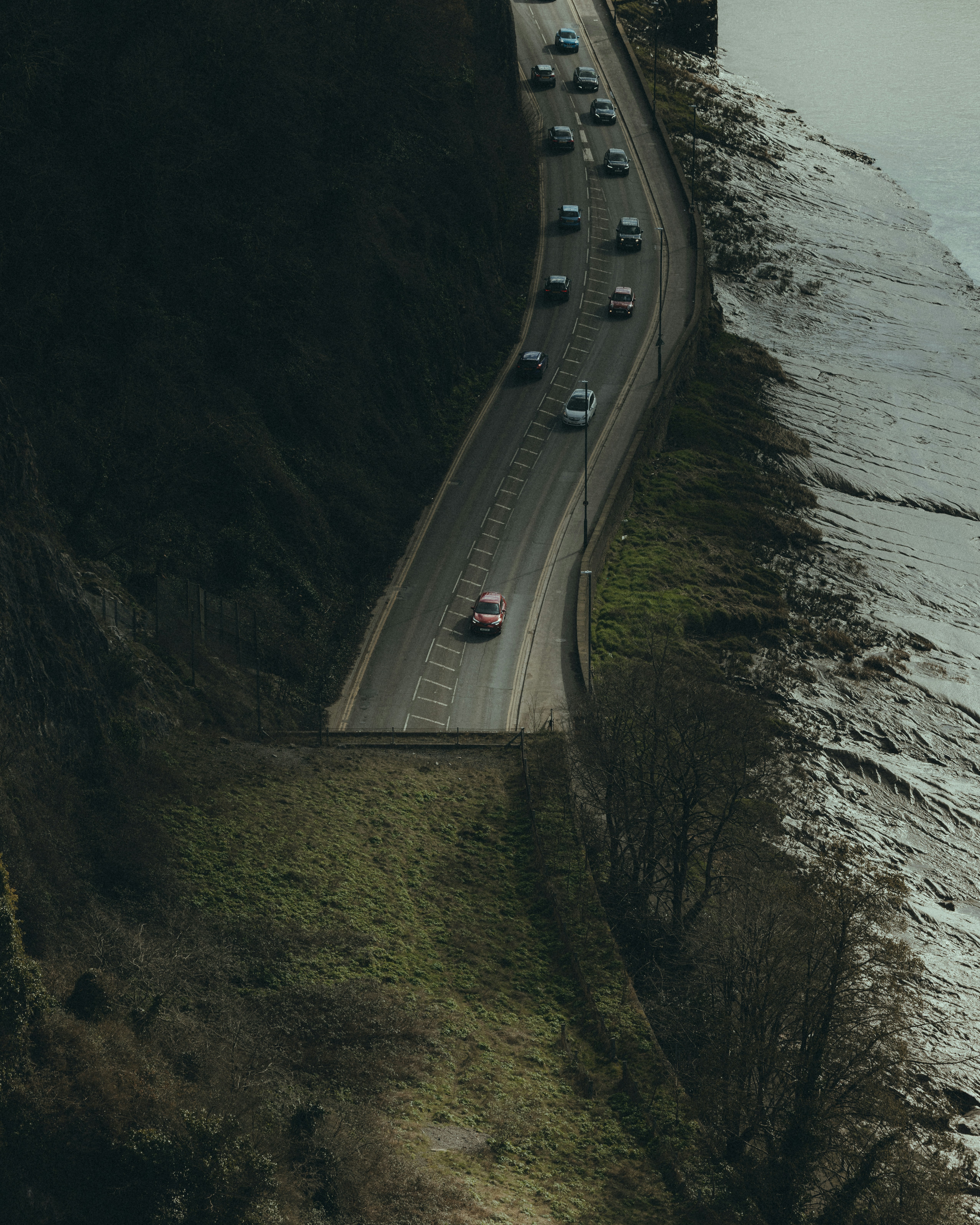 Cars drive along a scenic road by the sea.