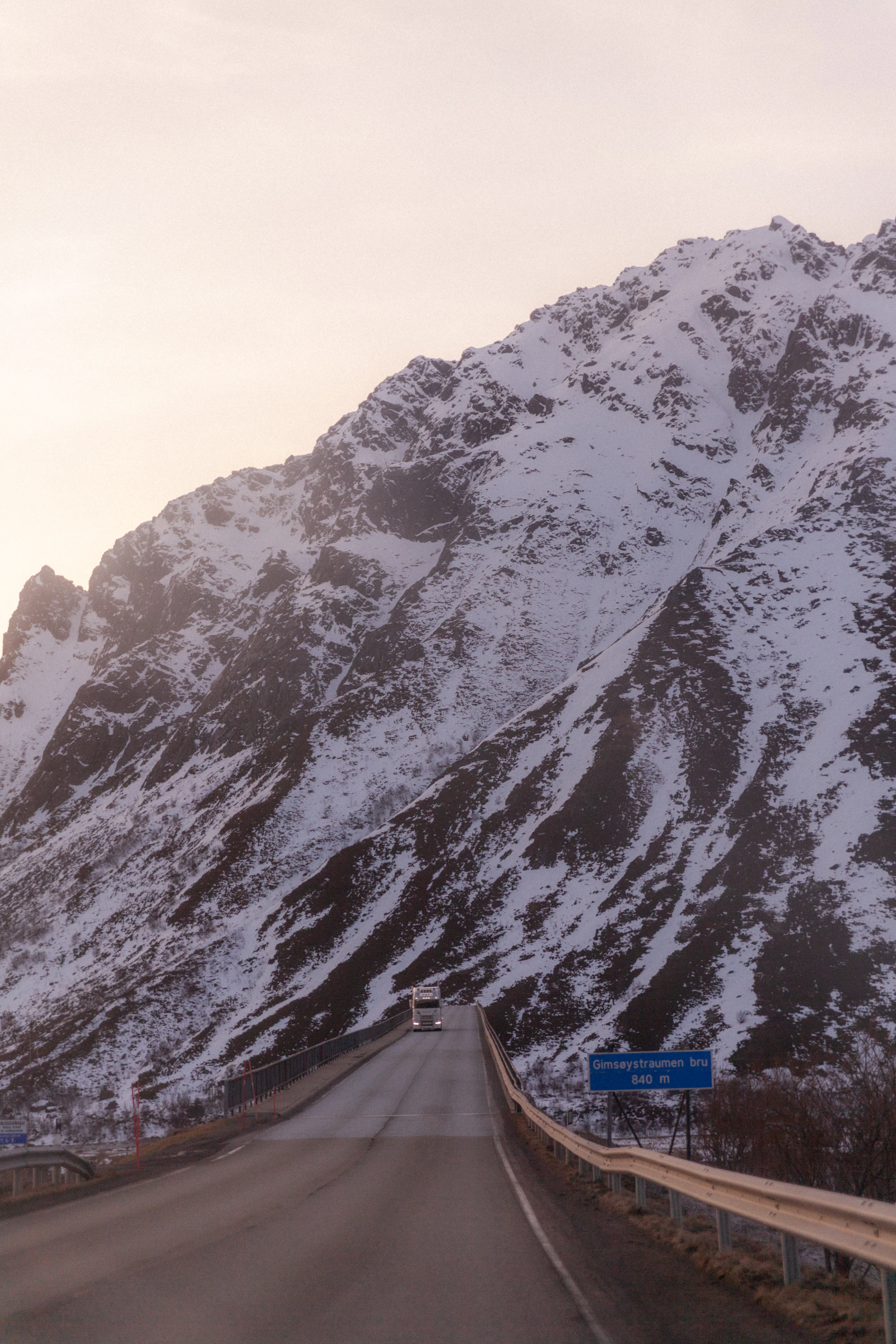 A vehicle travels toward a snowy mountain in Lofoten