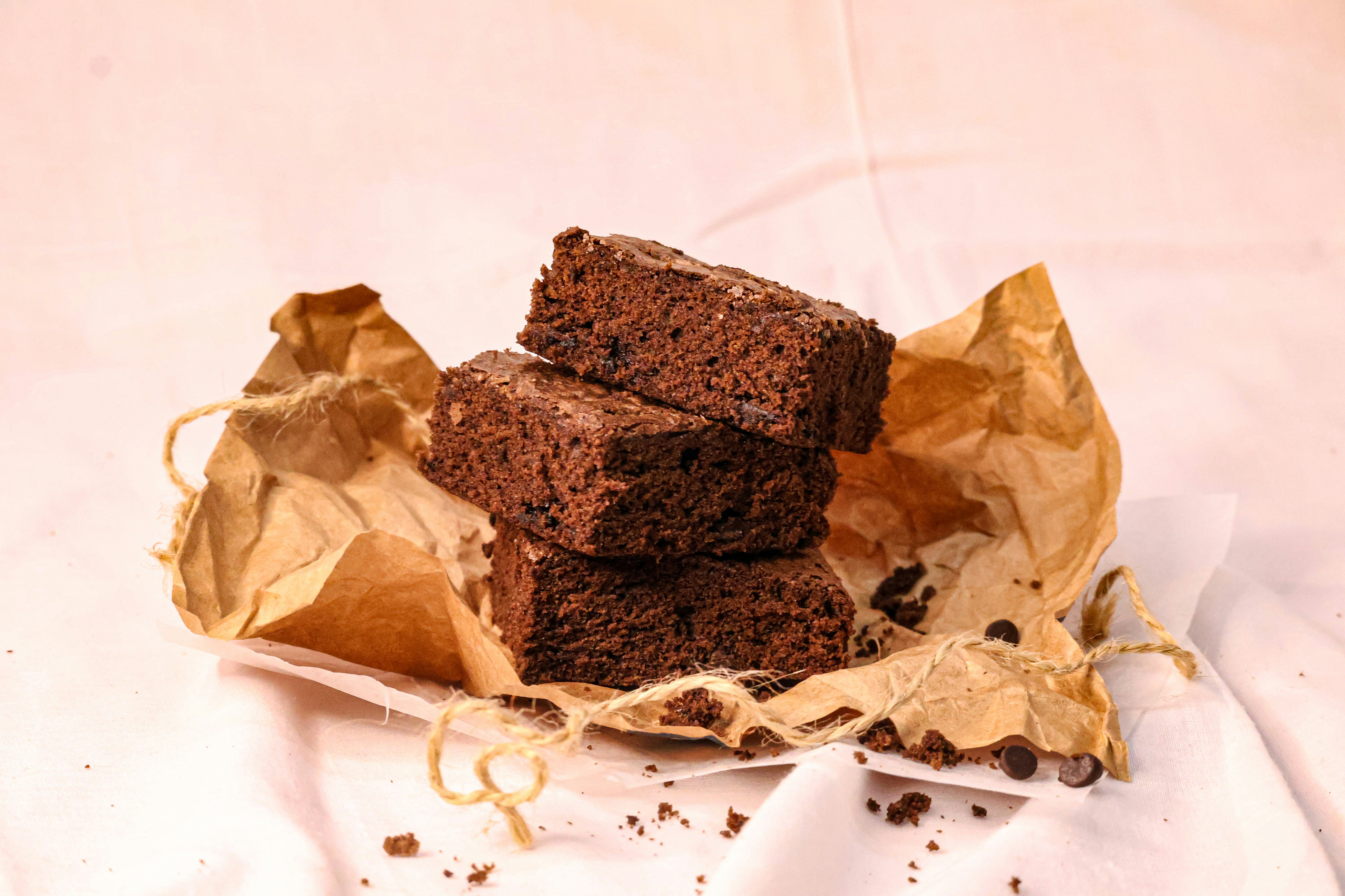 Brownies are stacked on brown paper.