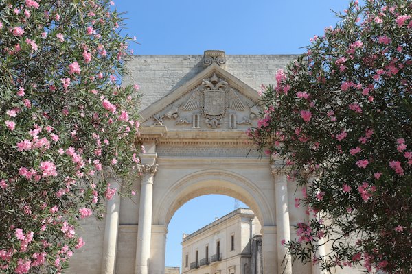 Ancient stone archway framed by pink flowers — Lecce, Italy