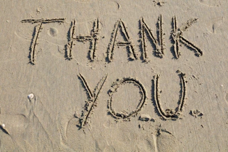 Thank you is written on the sand.