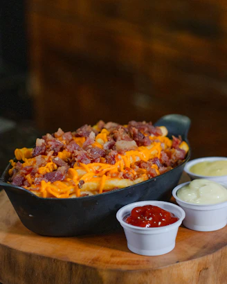 Fries topped with cheese and bacon, served with sauces.