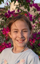 A smiling girl poses in front of pink flowers.