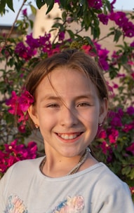 A smiling girl poses in front of pink flowers.