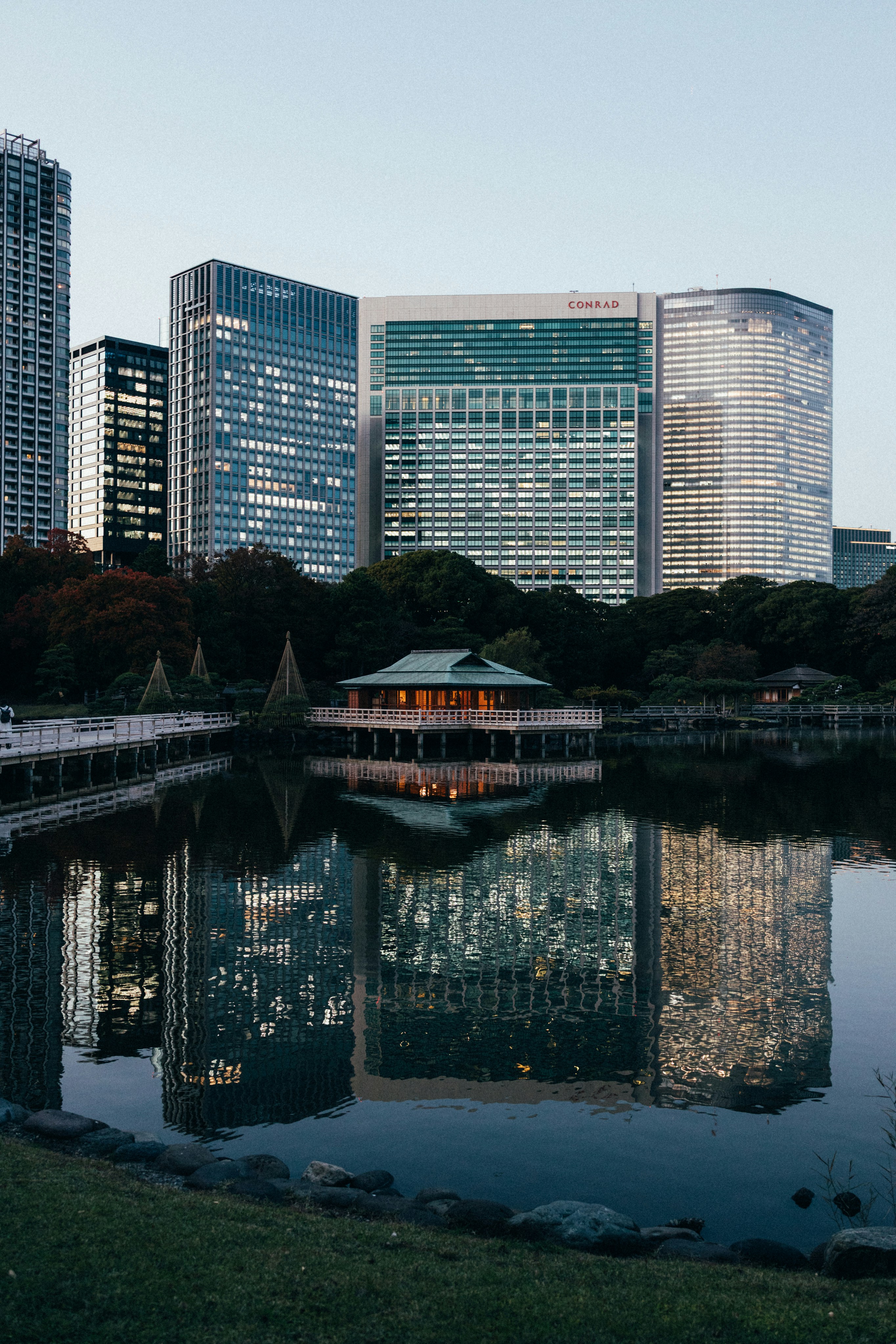 Buildings reflect in a pond, surrounded by skyscrapers.