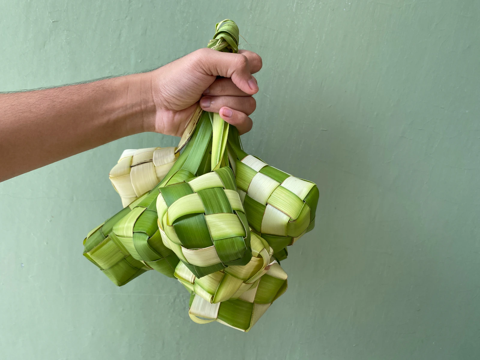 A pair of hands holding a bundle of woven ketupat, the rice cakes that mark Hari Raya in Malaysian homes