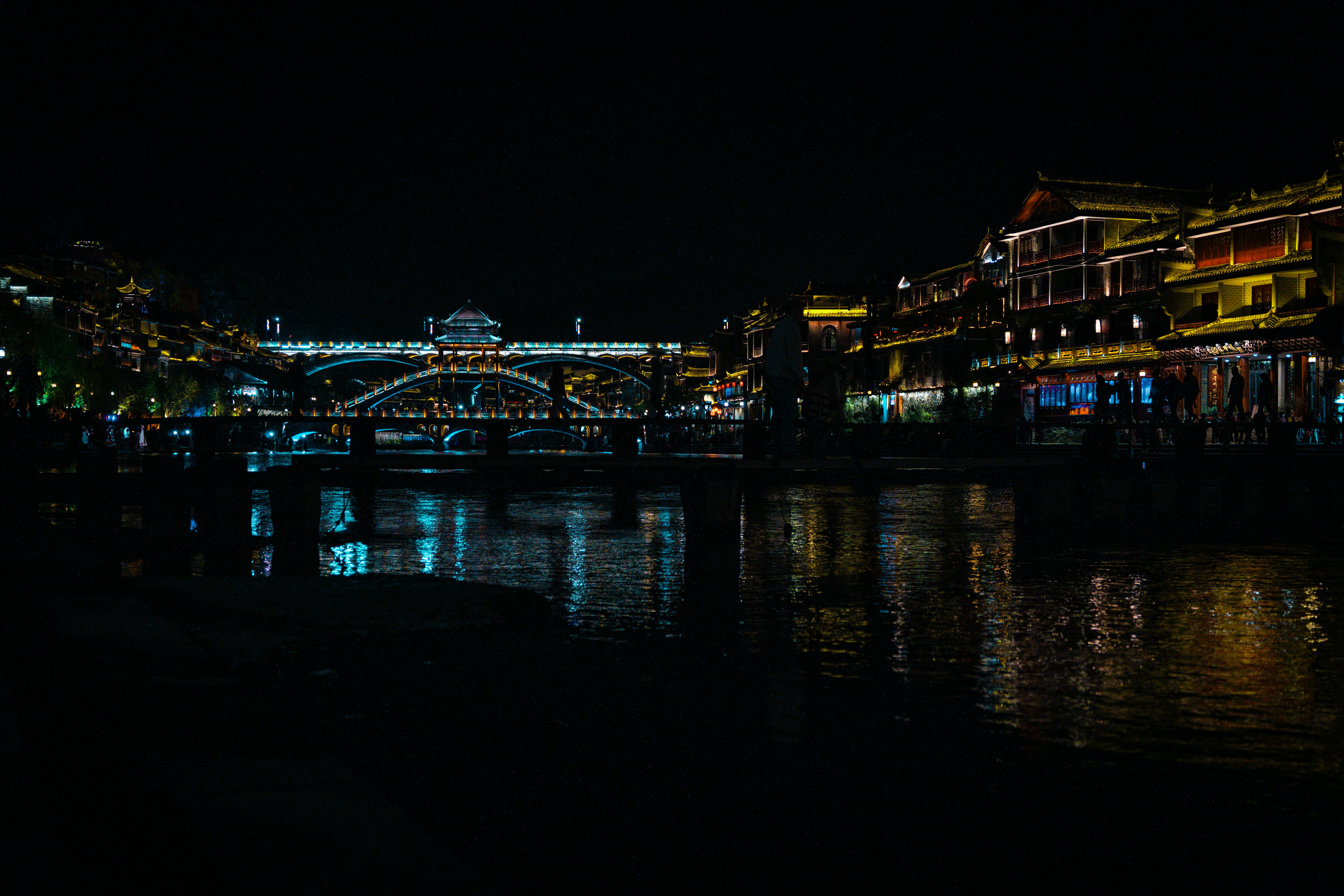 A lit-up cityscape reflects in the dark water.
