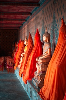 Buddha statues draped in orange cloth sit in a row.