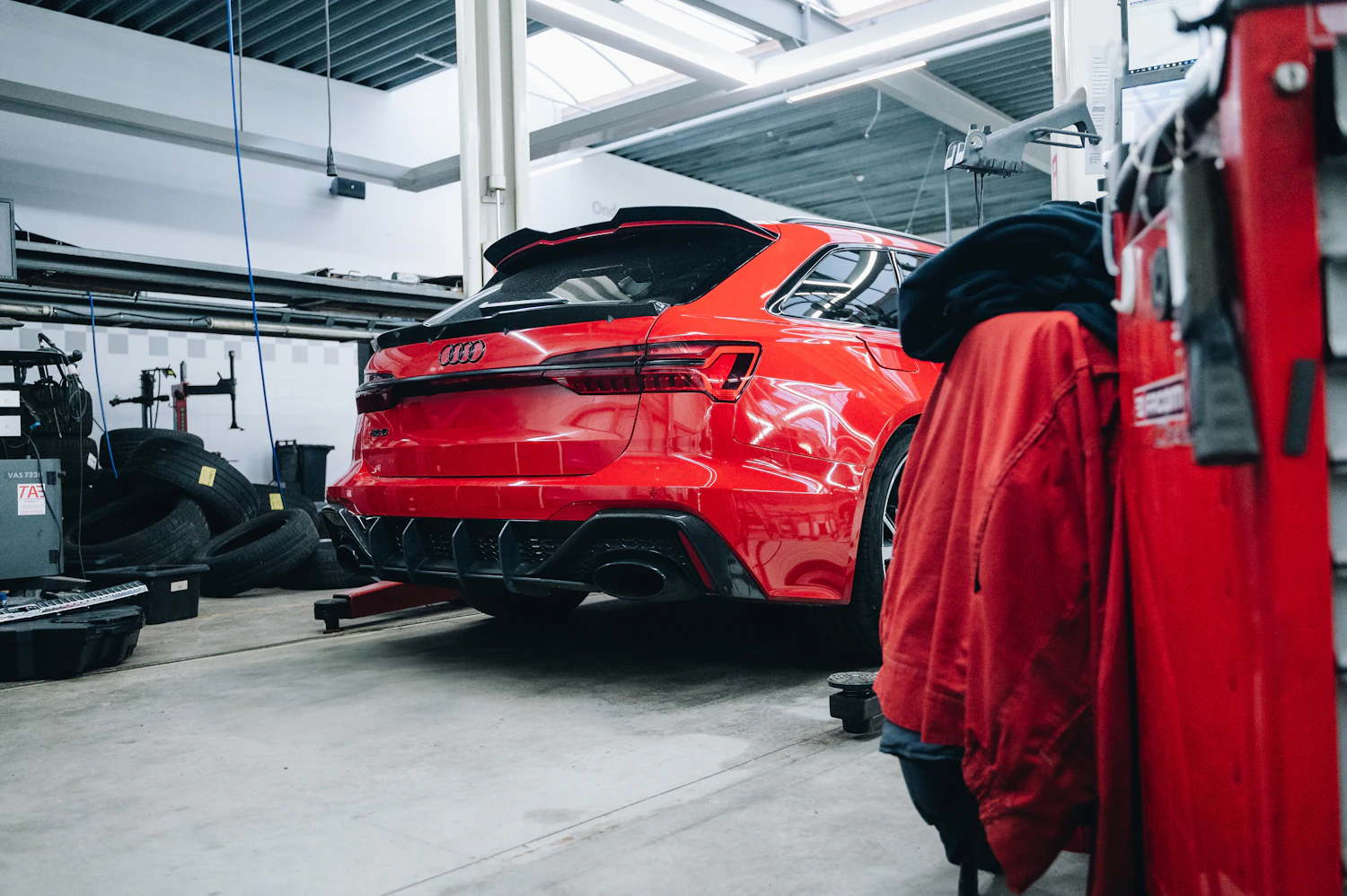 Coche rojo en un taller mecánico con zona de neumáticos y elevador