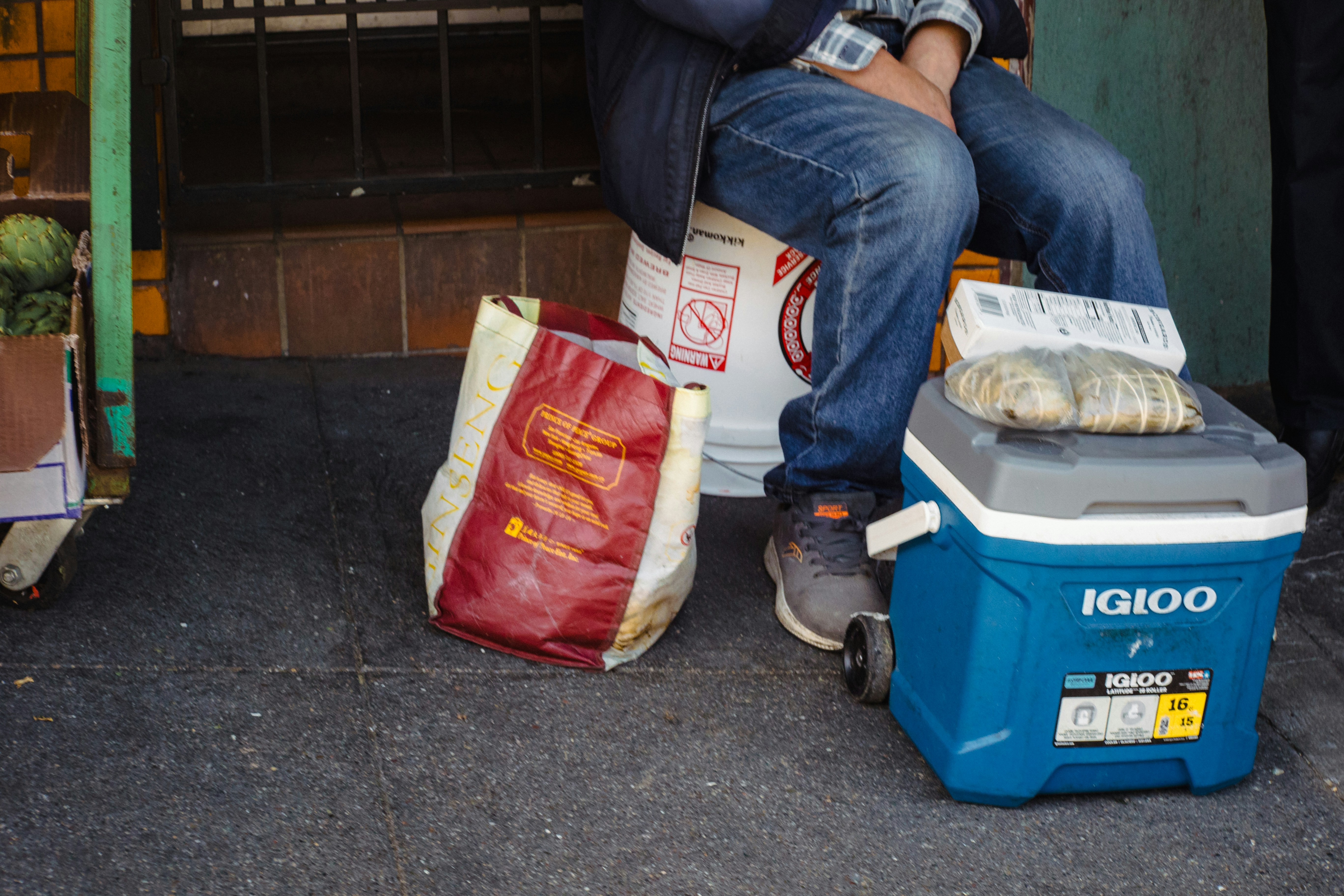 Person sits next to food and cooler outside.