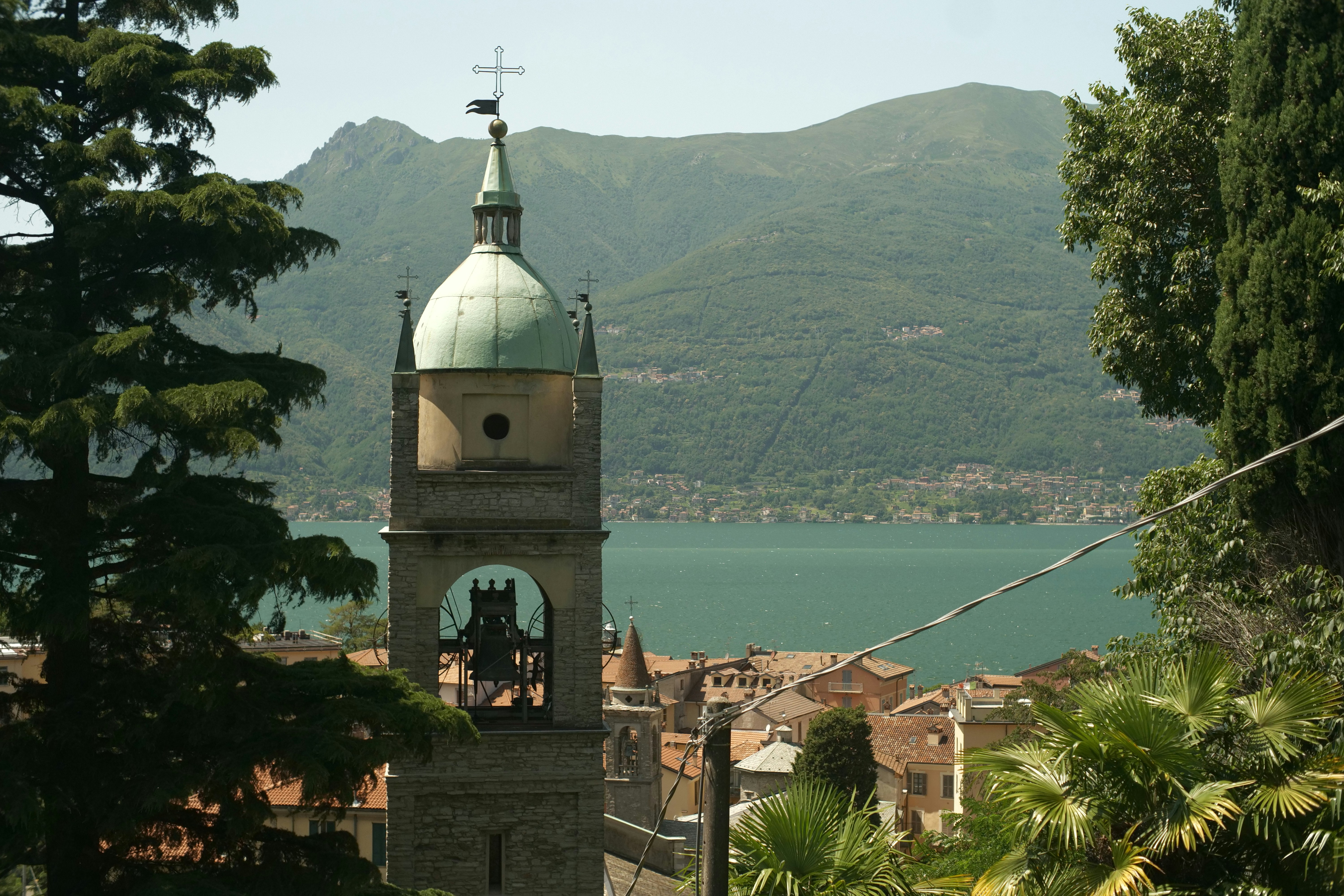 A church bell tower looks over water and mountains.