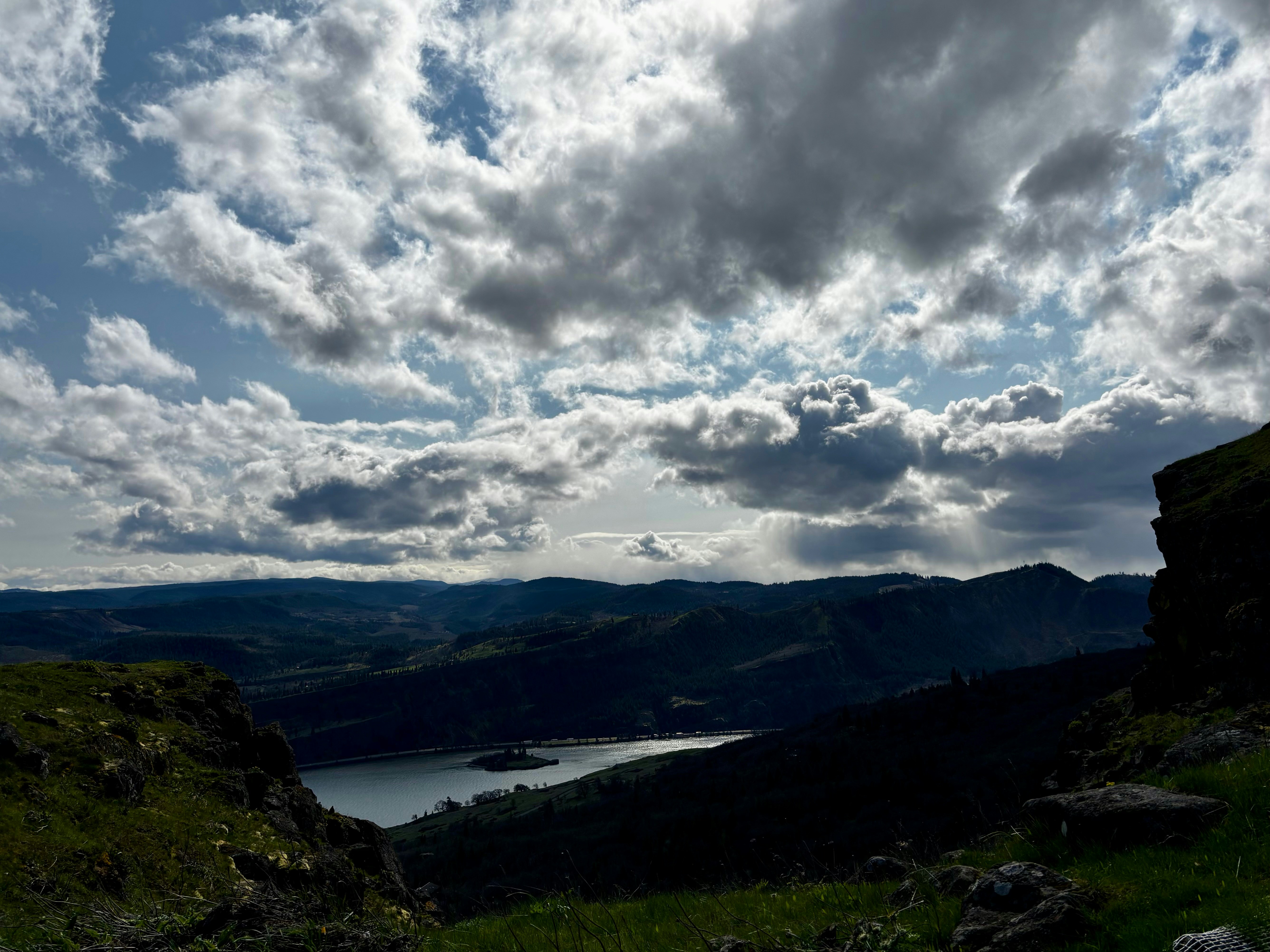Dramatic clouds hover over mountains and a lake.