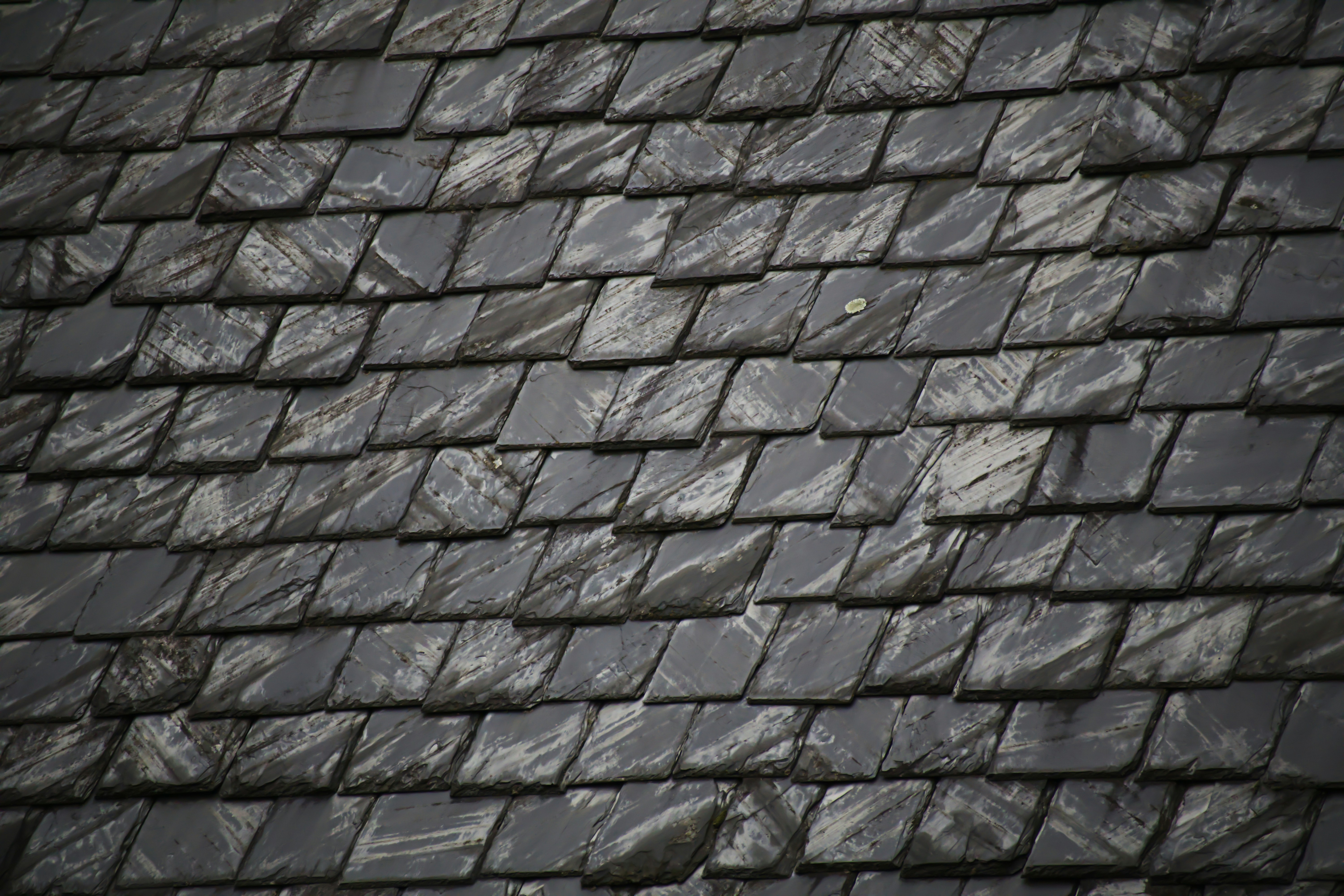 professional roofer replacing a cracked slate tile using specialized tools - how much does it cost to repair a slate roof