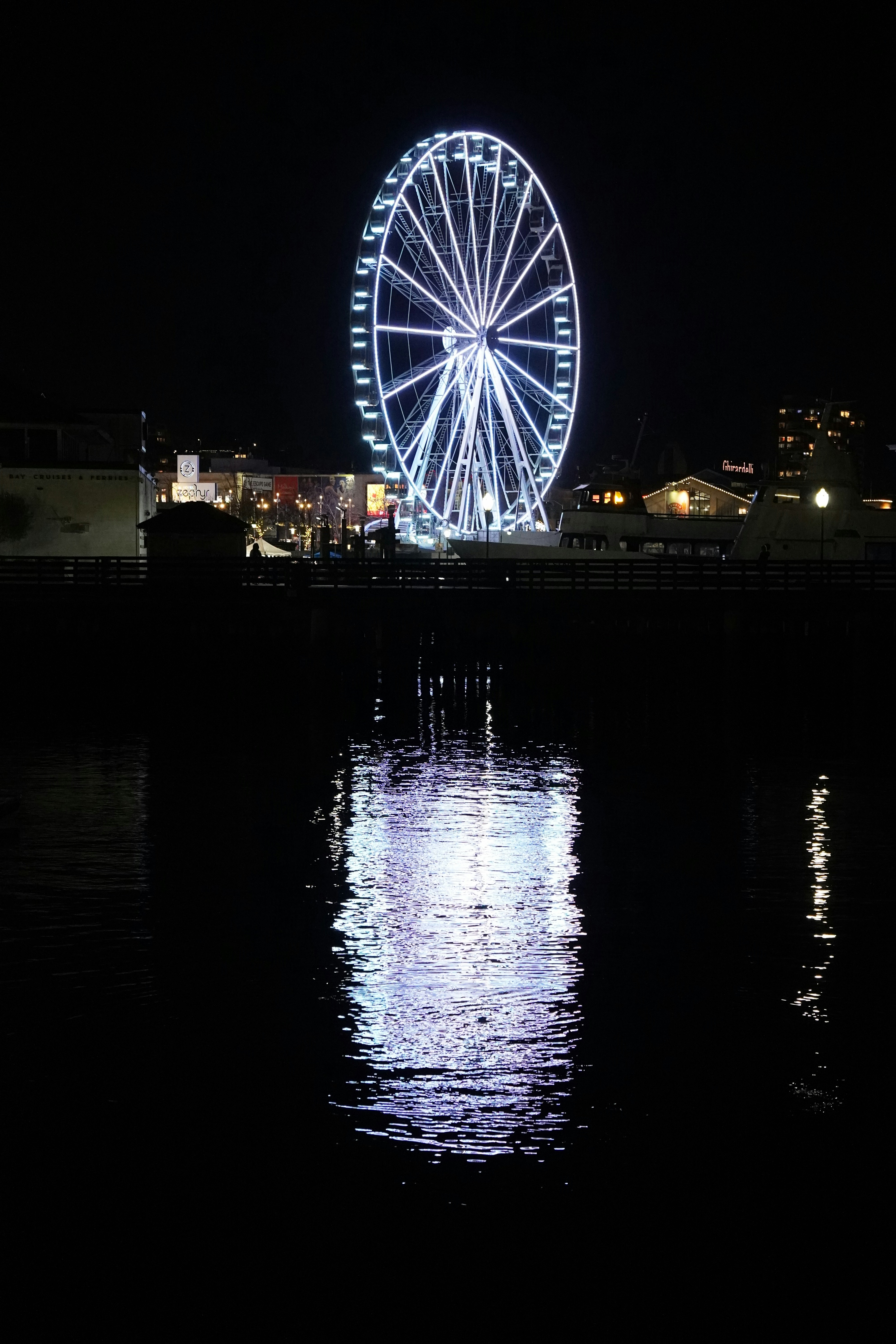 A glowing ferris wheel reflects on the water.