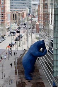 A blue bear statue looms over a city street.