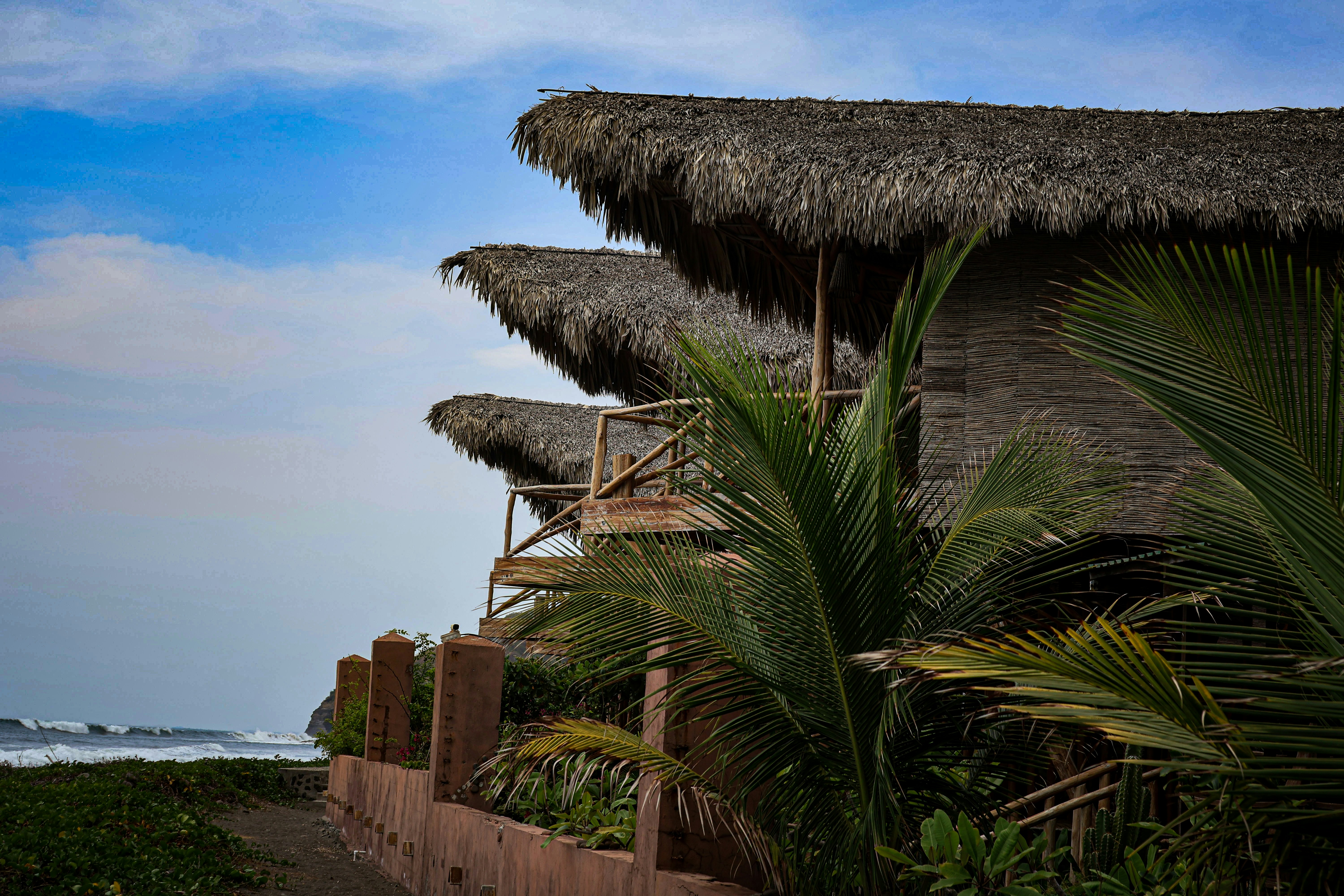 Cabins with thatched roofs sit near the ocean.