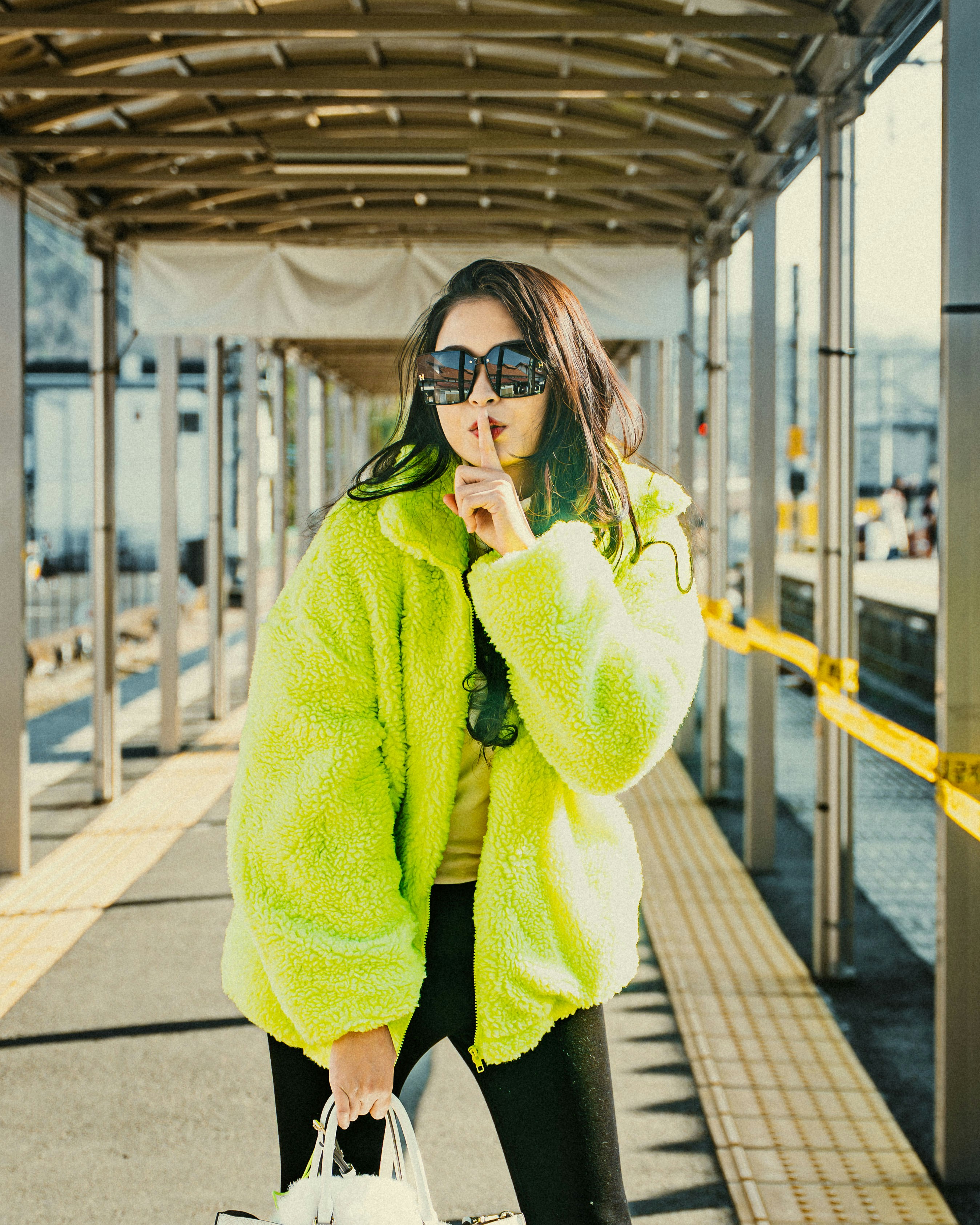 Woman makes a "shhh" gesture while wearing neon green jacket.
