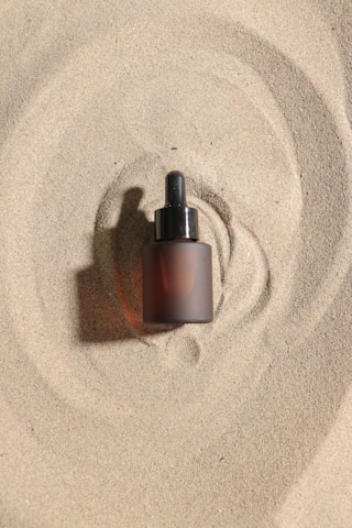 A bottle of serum sits on the sand.