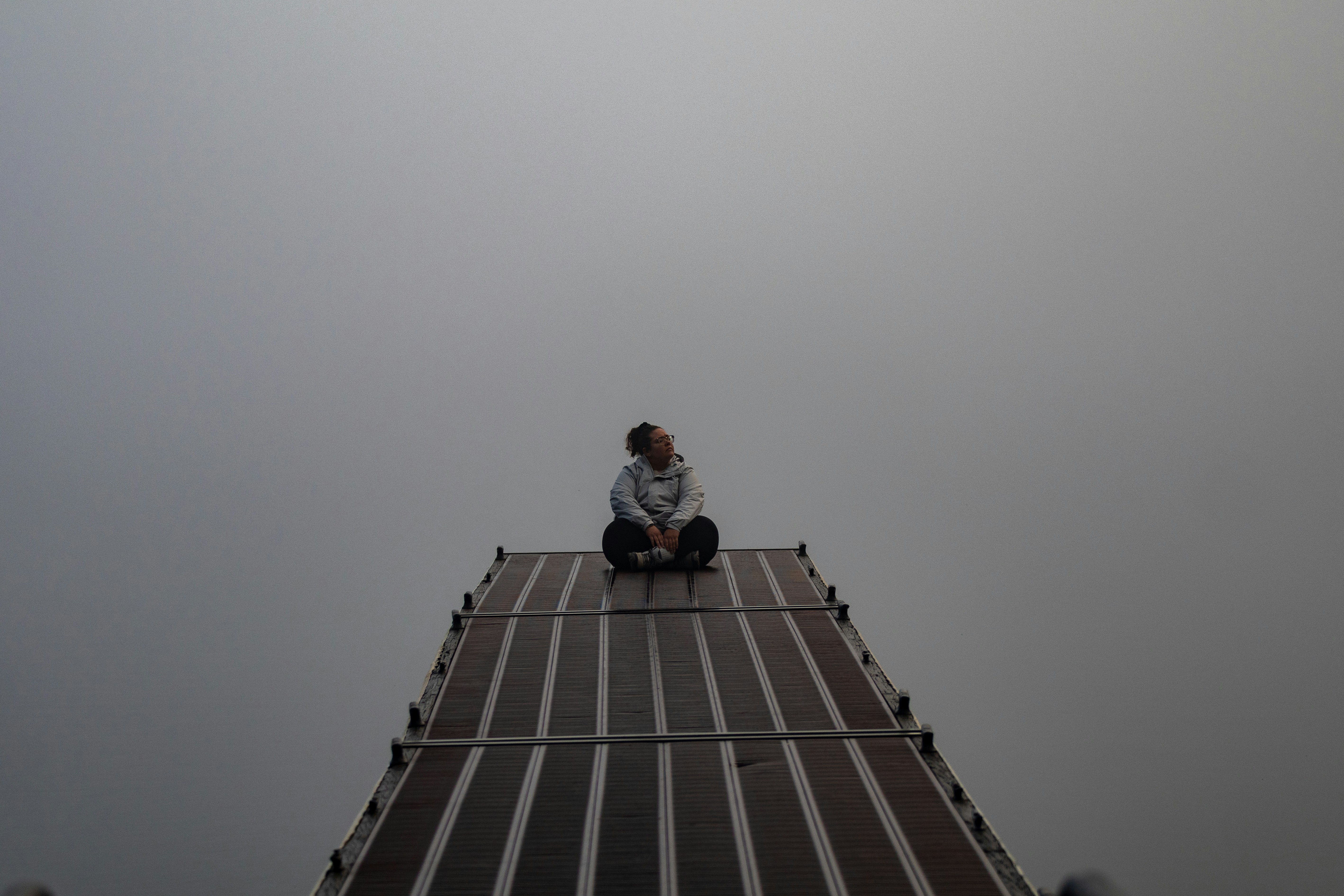 A person sits atop a structure, surrounded by fog.