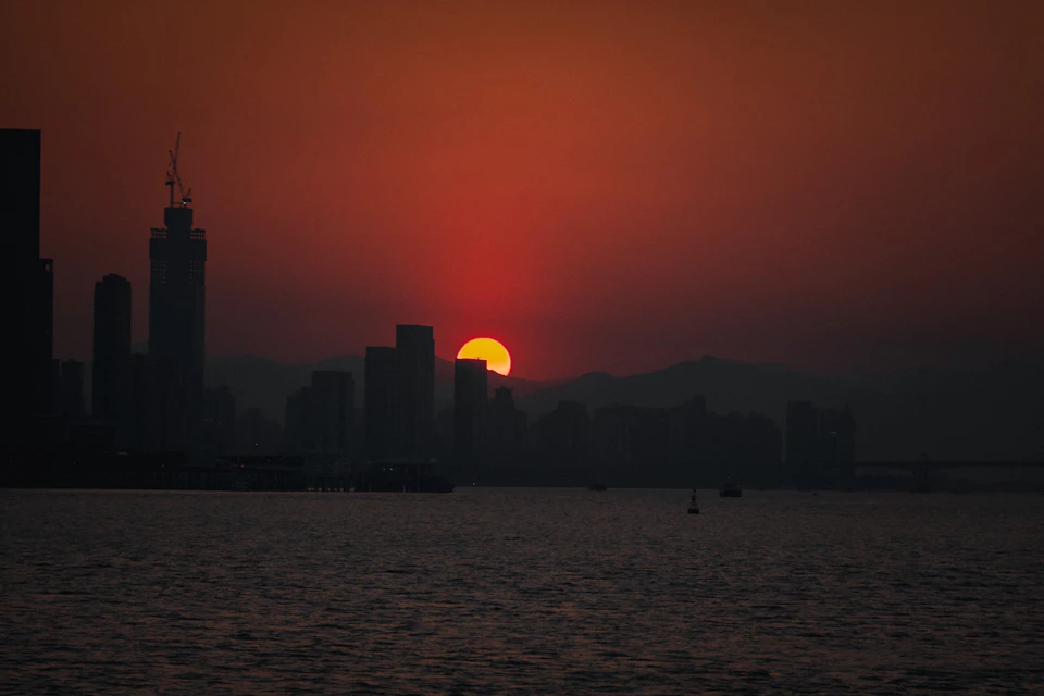 City skyline at sunset with warm glow over urban landscape and boats on water