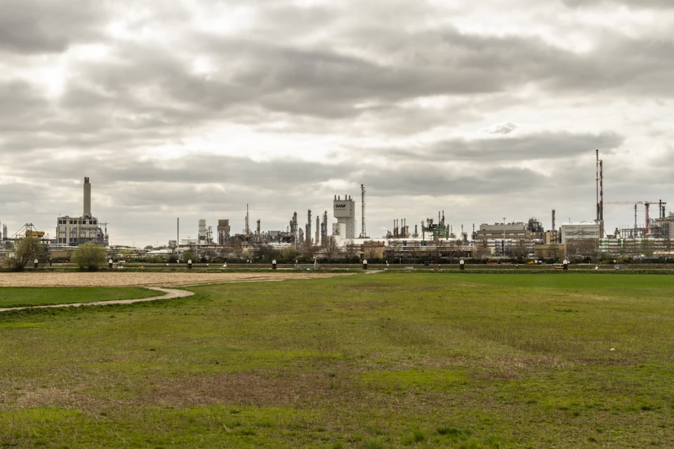 The image depicts a large industrial complex with multiple power plants and smokestacks, situated on a vast expanse of land. The sky above is filled with clouds, casting a soft light over the scene. In the foreground, there are several buildings that appear to be part of the complex, including a factory and a power plant. The image is taken from a distance, providing a comprehensive view of the industrial landscape.