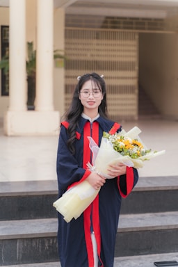 A graduate smiles, holding flowers, ready to celebrate.