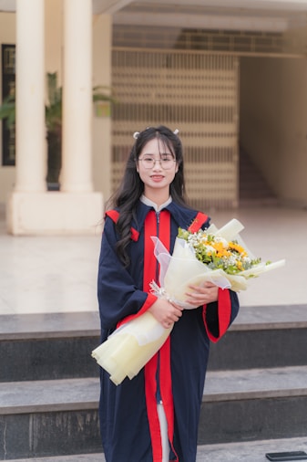 A graduate smiles, holding flowers, ready to celebrate.