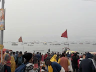 People gather near a river, with boats on it