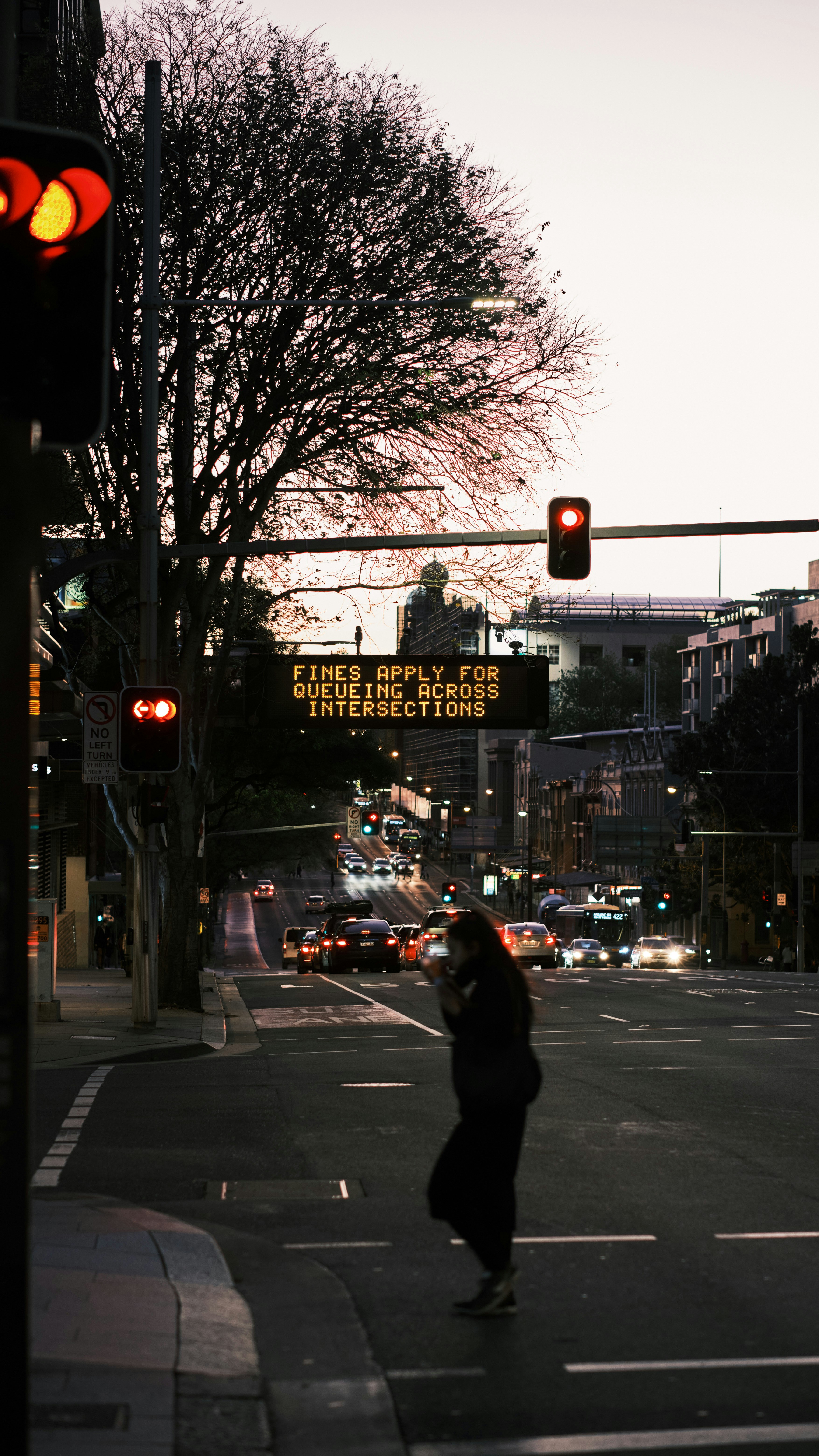 A person crosses street at dusk, near traffic lights.