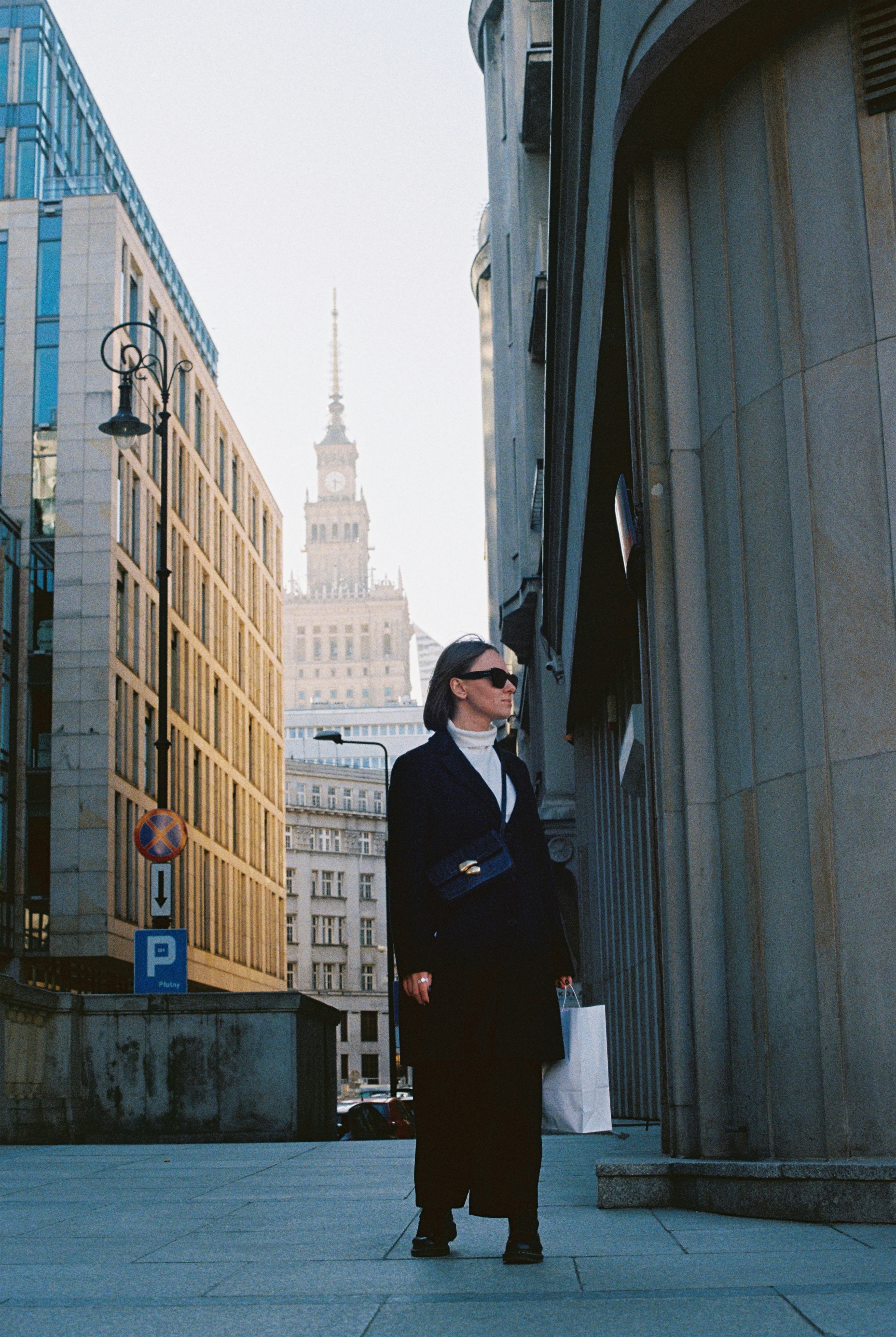 Woman walks down a city street wearing a jacket.