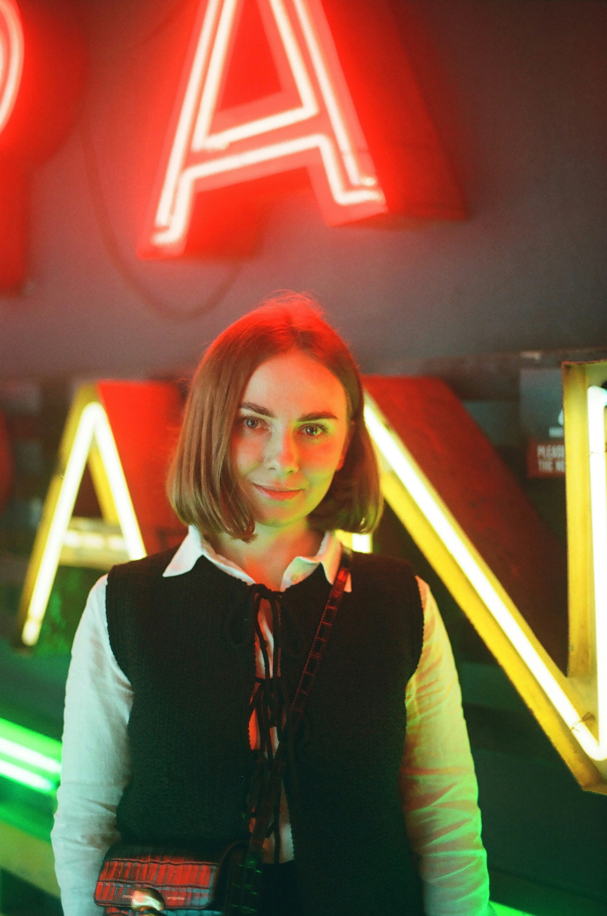Young woman poses under neon signs.