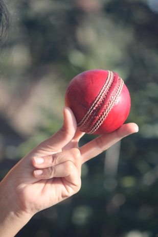 A hand holds up a red cricket ball.