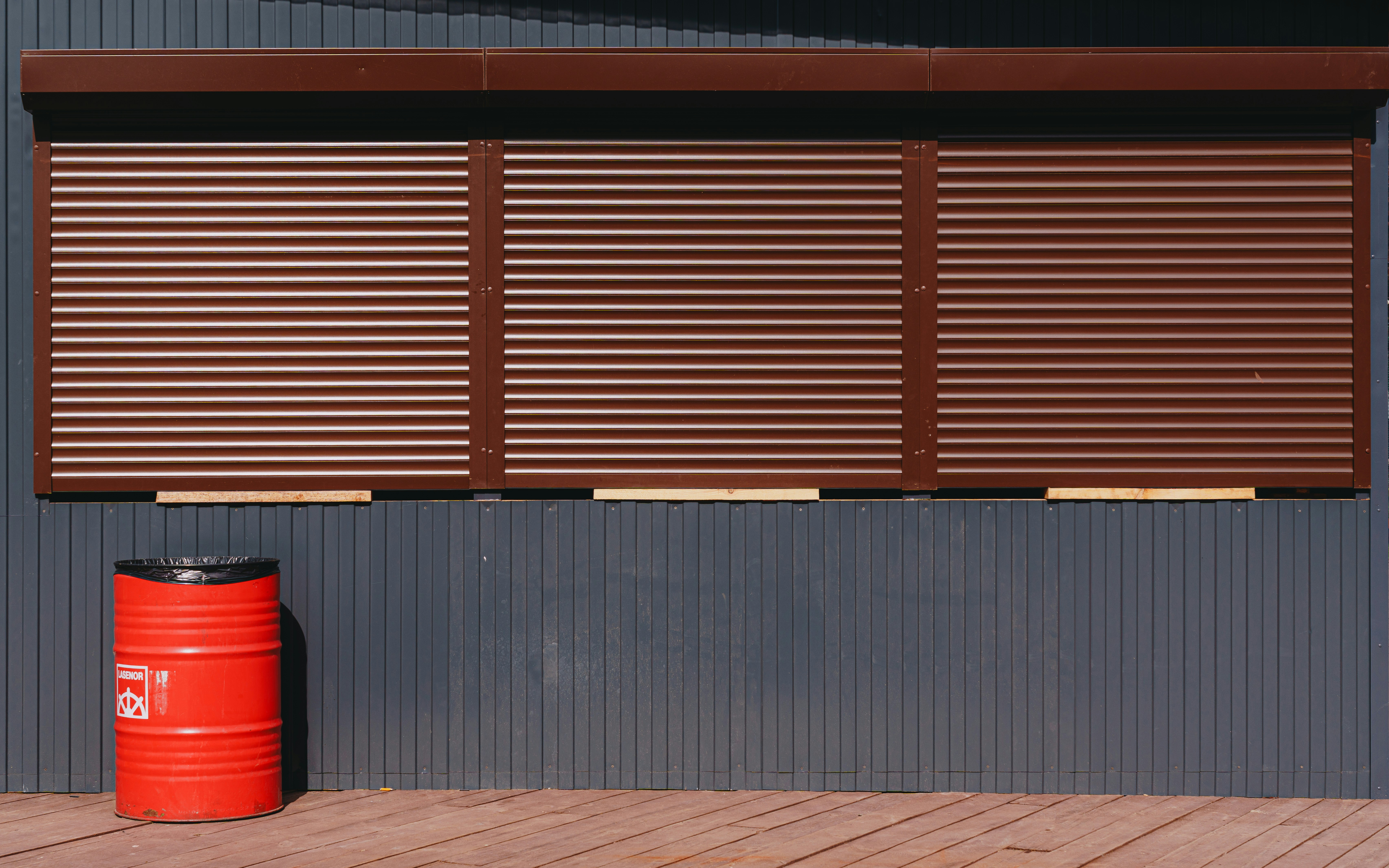 Brown shutters and a red barrel sit outside
